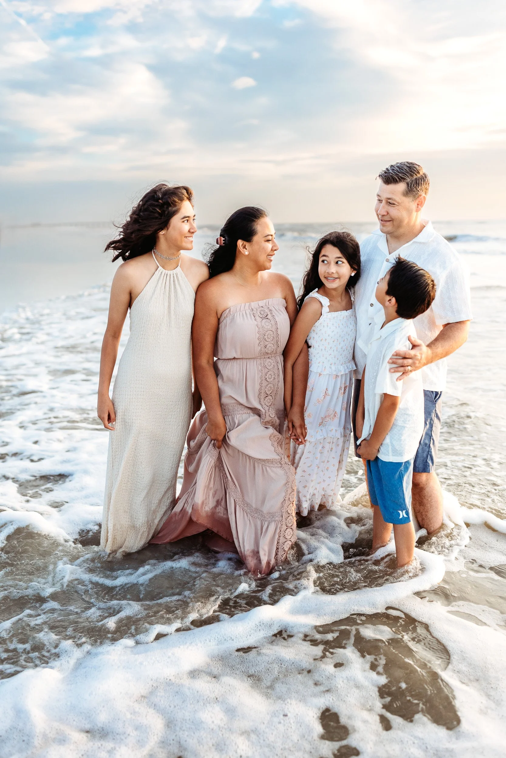 family embraced while standing in the water at Villano beach and they are laughing as a wave crashes around them