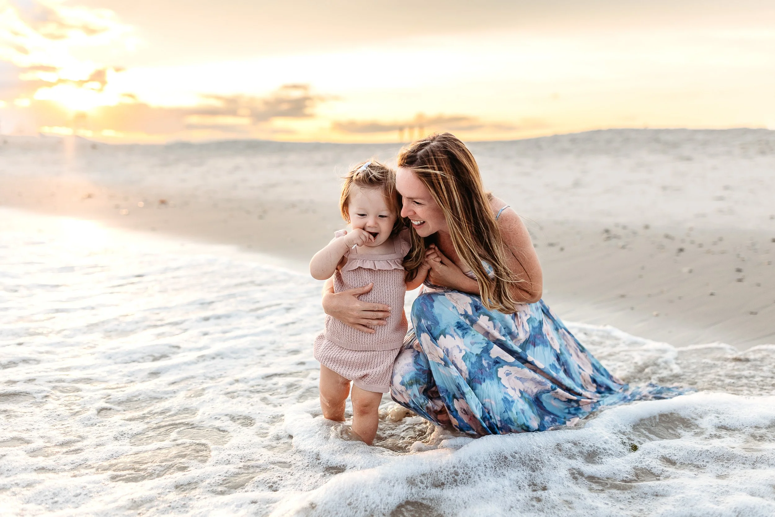 mother in the ocean with her toddler girl and they are laughing and it is sunset on the beach in st augustine and they are having family photos taken in a natural and relaxed way