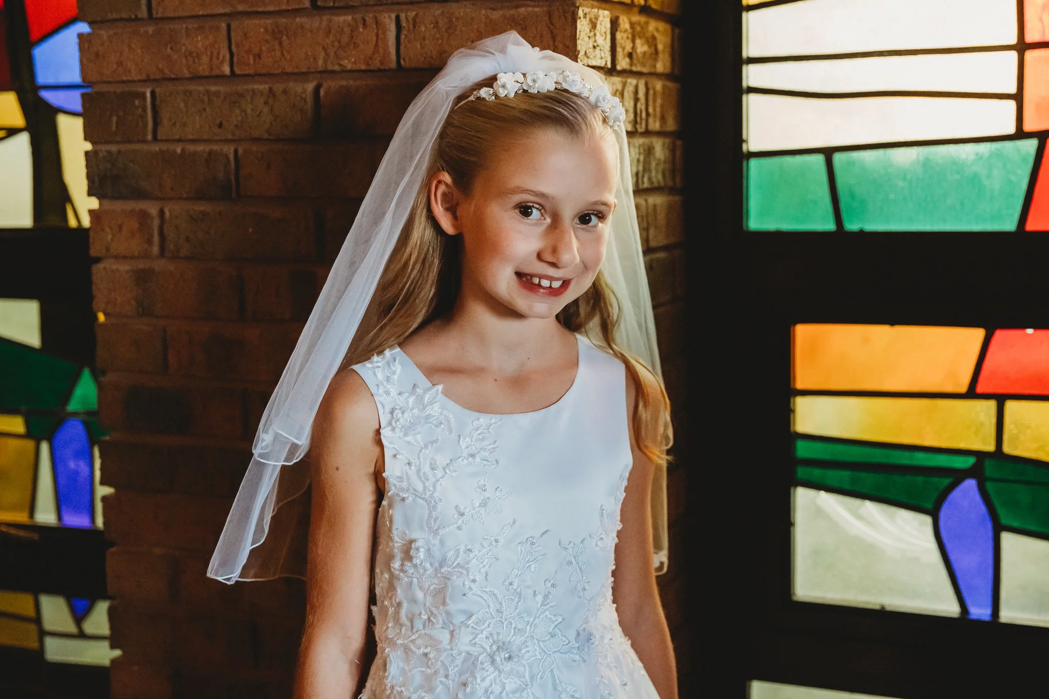 girl in communion dress in front of stained glass church window on communion day