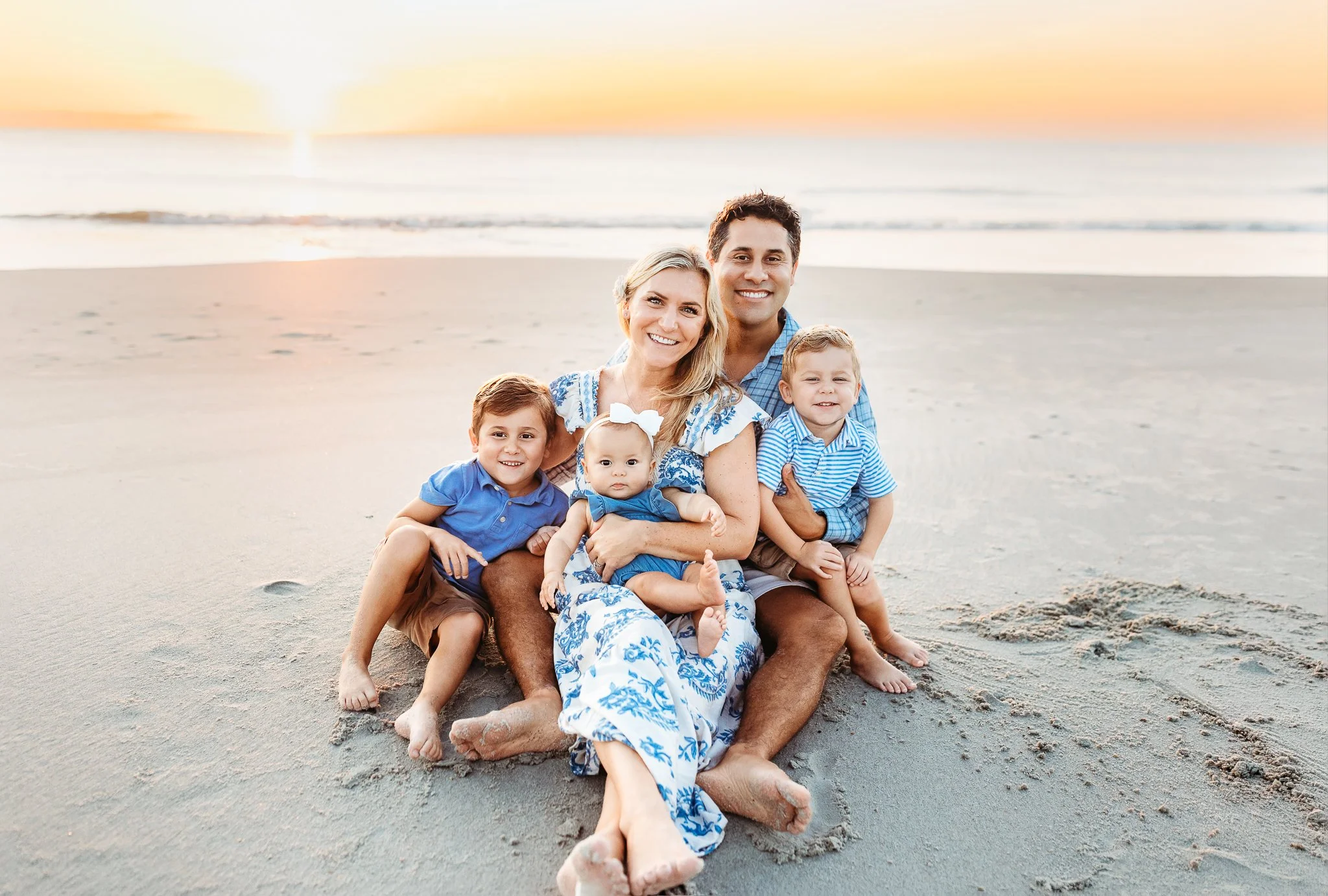 family seated on the sand at sunrise for a family portrait