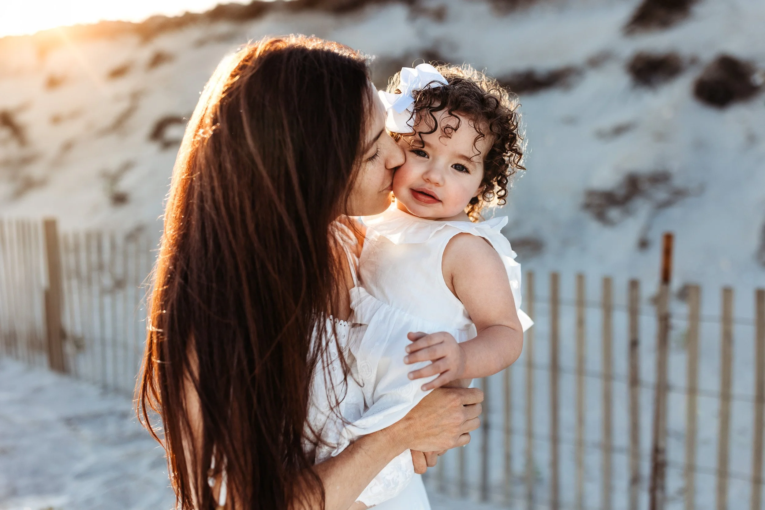 mom kissing baby girl at sunset and she is looking at camera
