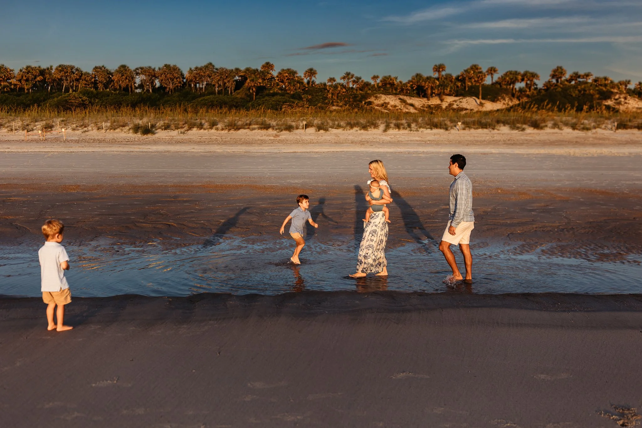 family walking tough a puddle at ticklers beach with golden sun spotlighting them