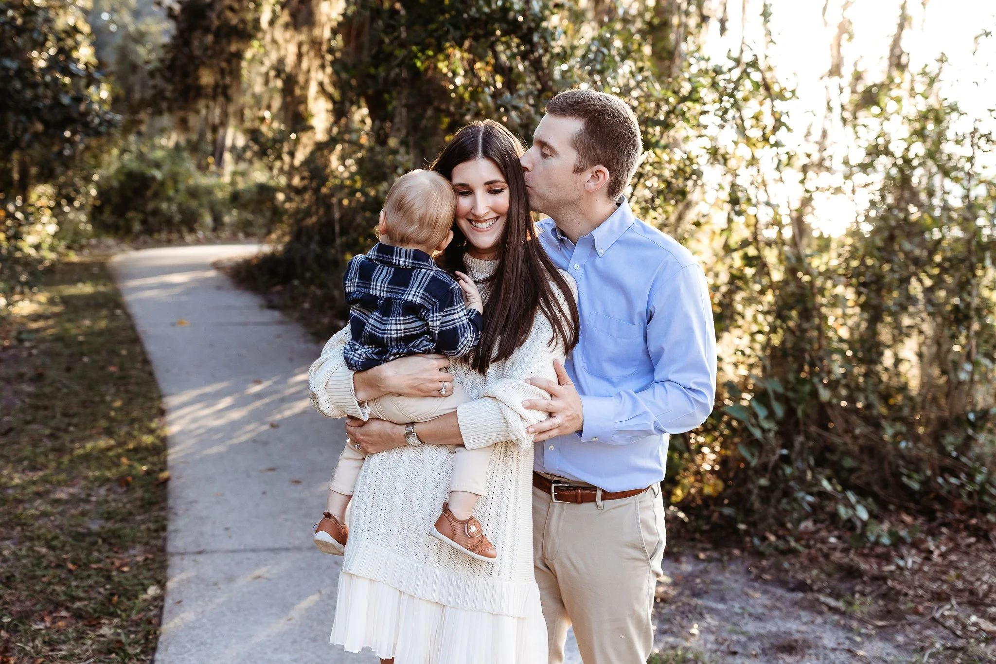 husband kissing wife on the Cheek who is holding her baby