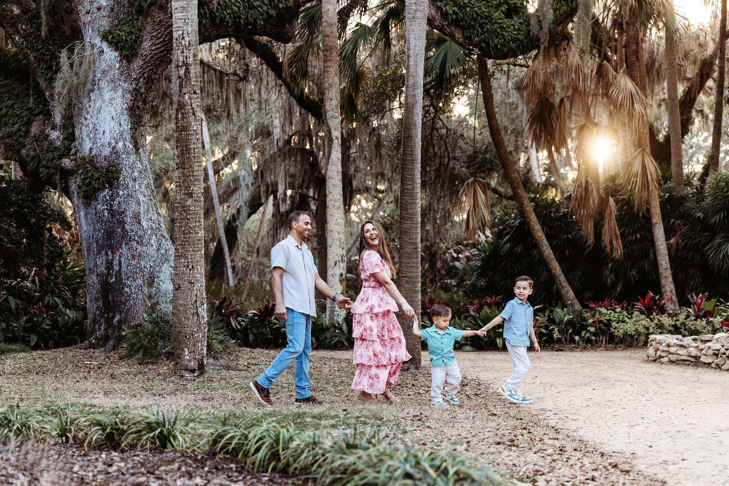 family walking in a garden and the sun is shining through the oak trees and they are single file hand in hand at Washington oaks garden