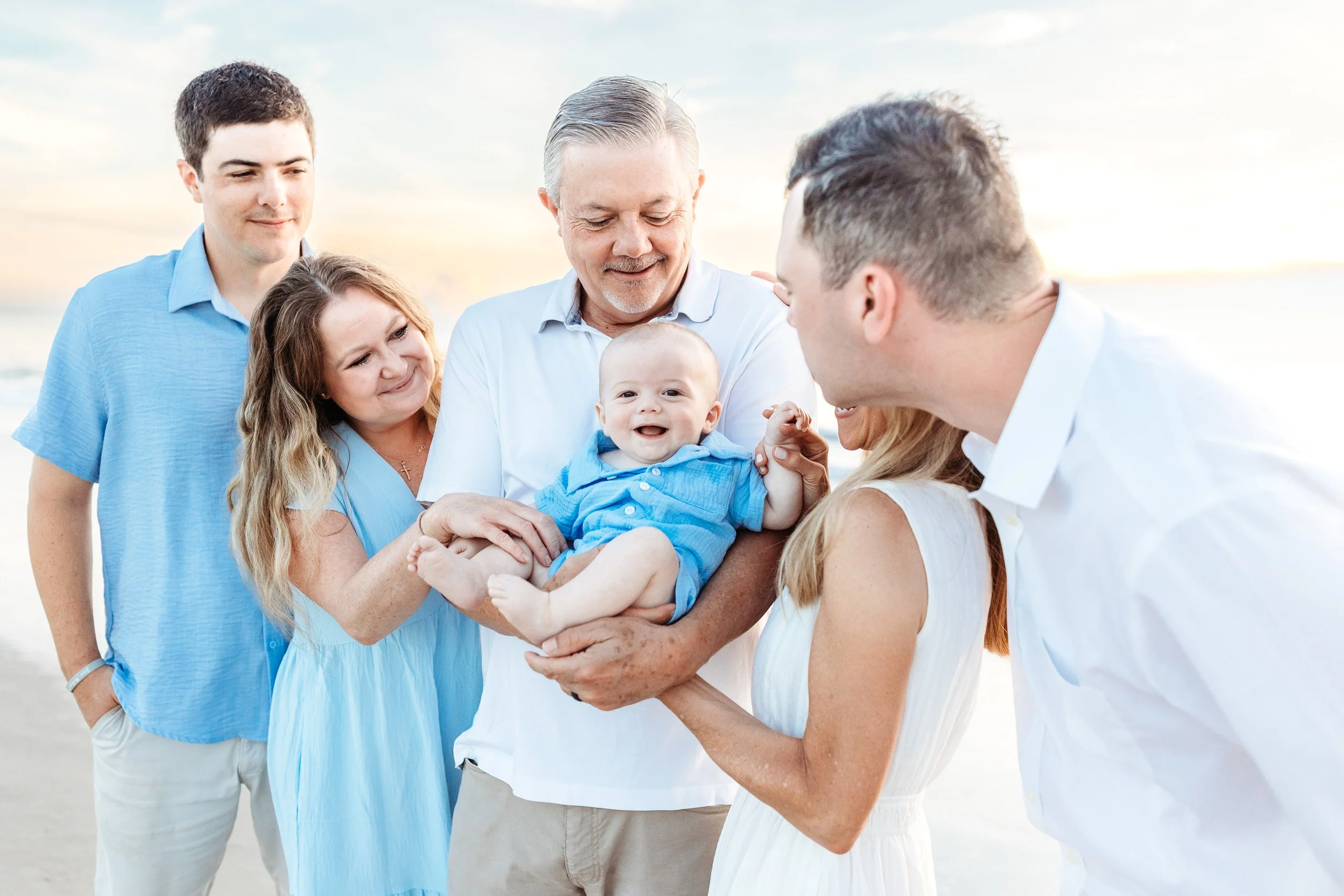 family surrounding a baby who is laughing on the beach in st augustine for family vacation photo session