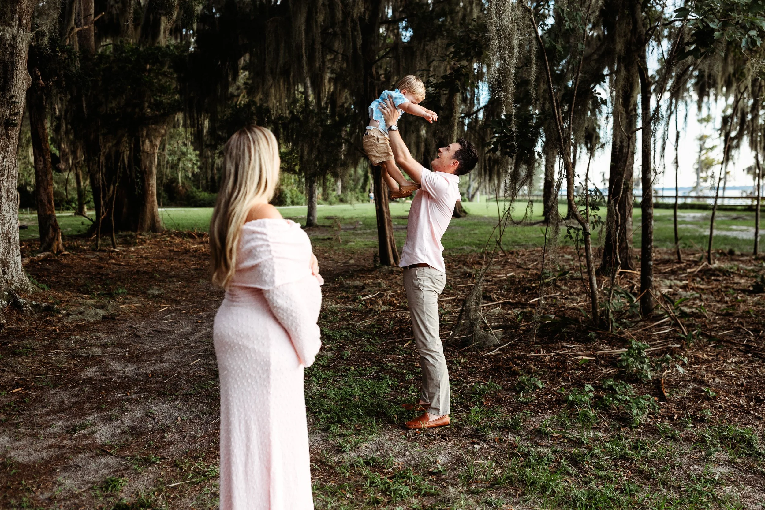 dad lifting child in the air while mom is in foreground watching