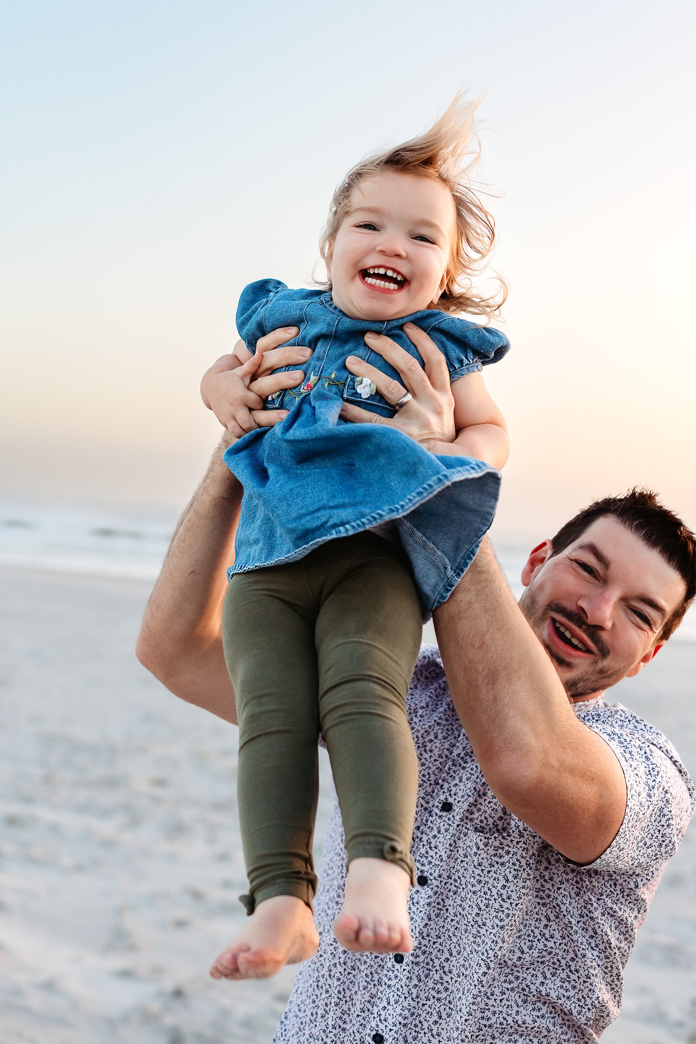 Smiling toddler being held by his father during a playful sunrise beach photography session in Crescent Beach.