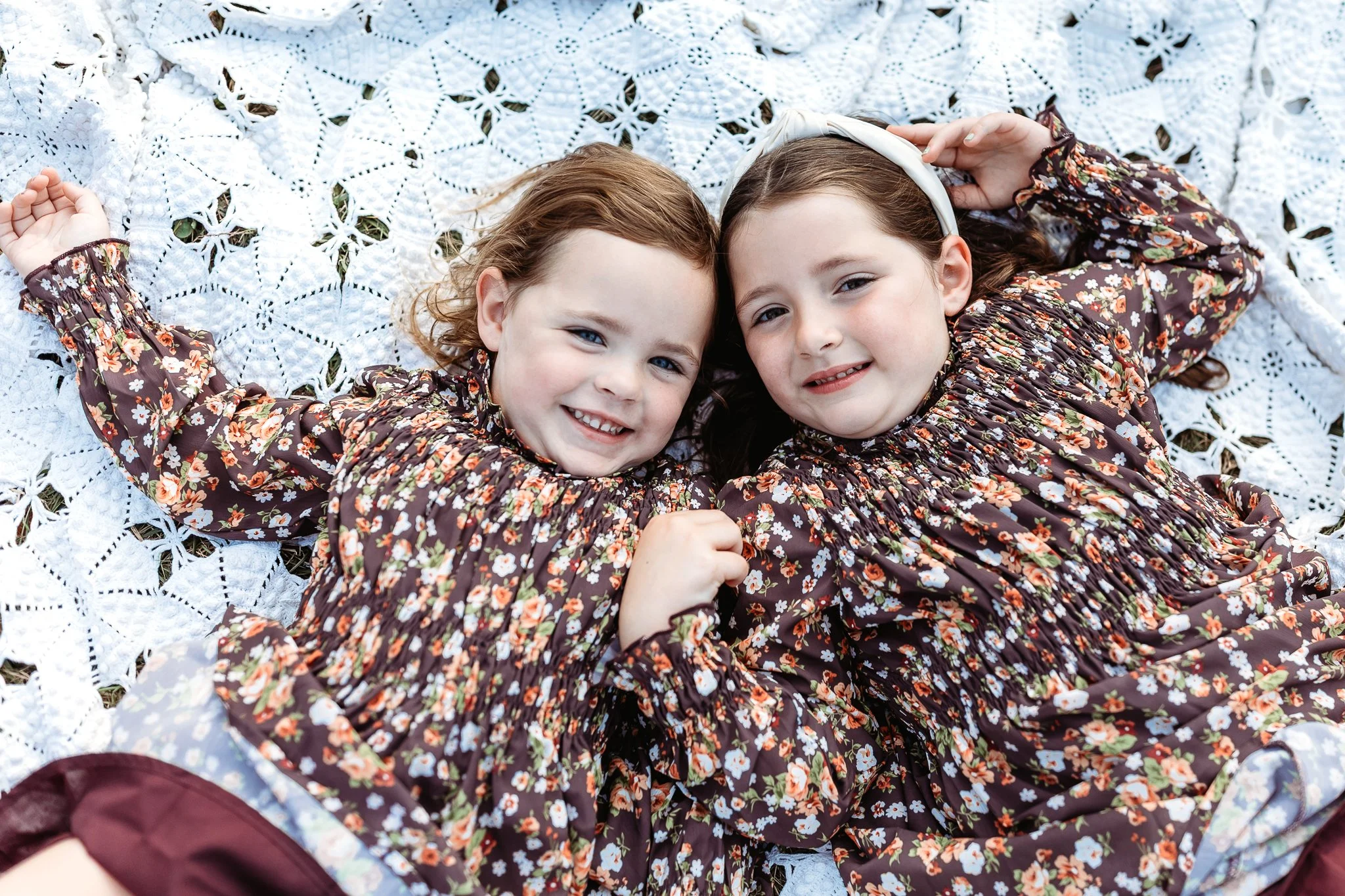 kids laying on a blanket in brown floral dresses laughing