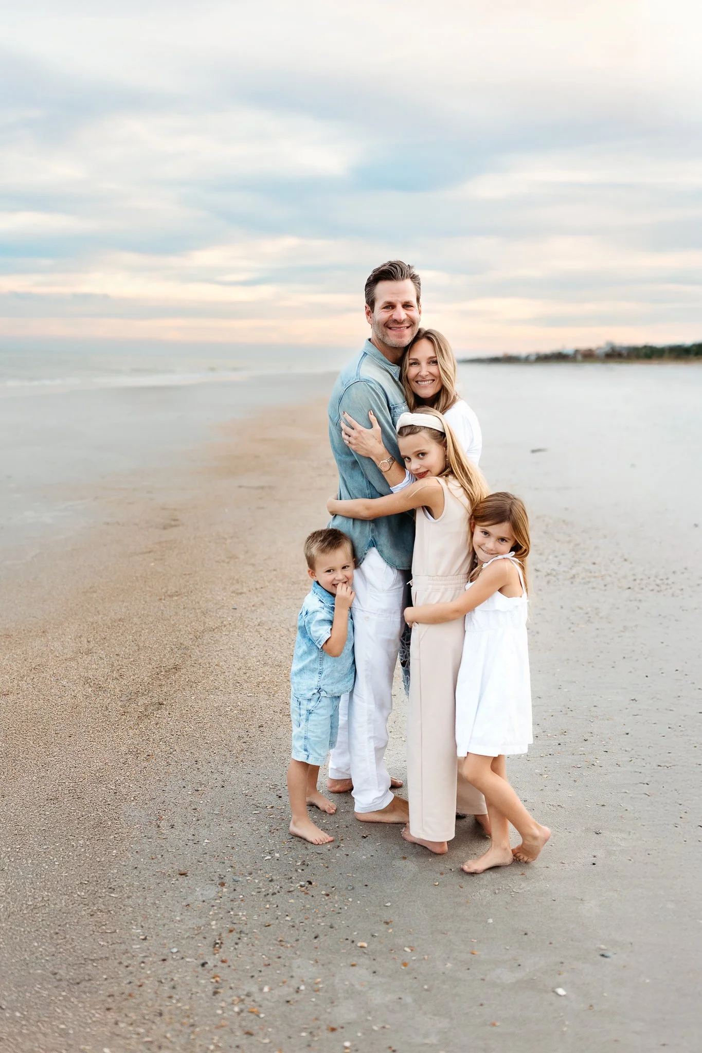 family with toddler aged children embraced on the beach at sunset