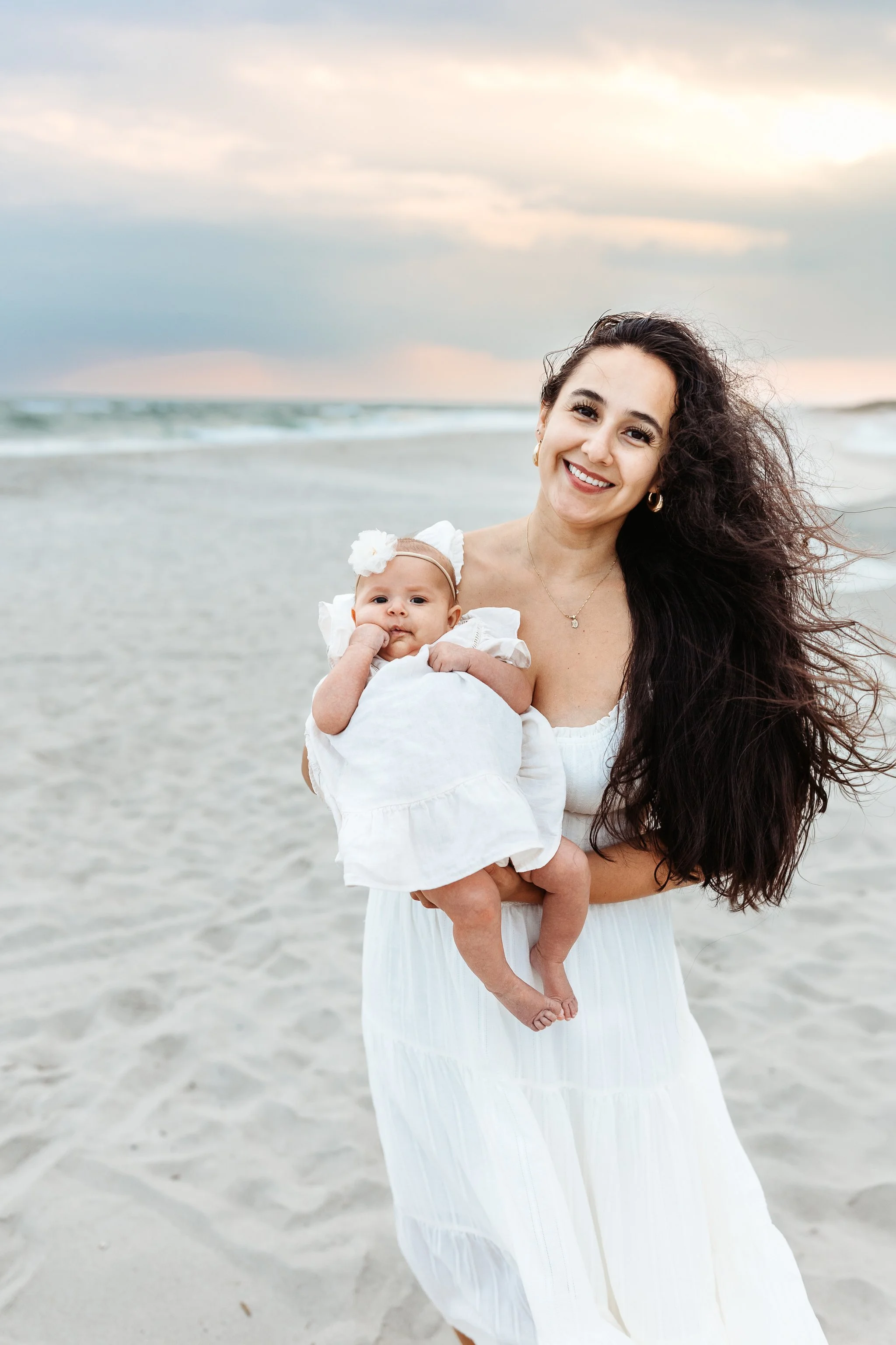 mother on the beach at sunset holding baby and they are both looking at the camera
