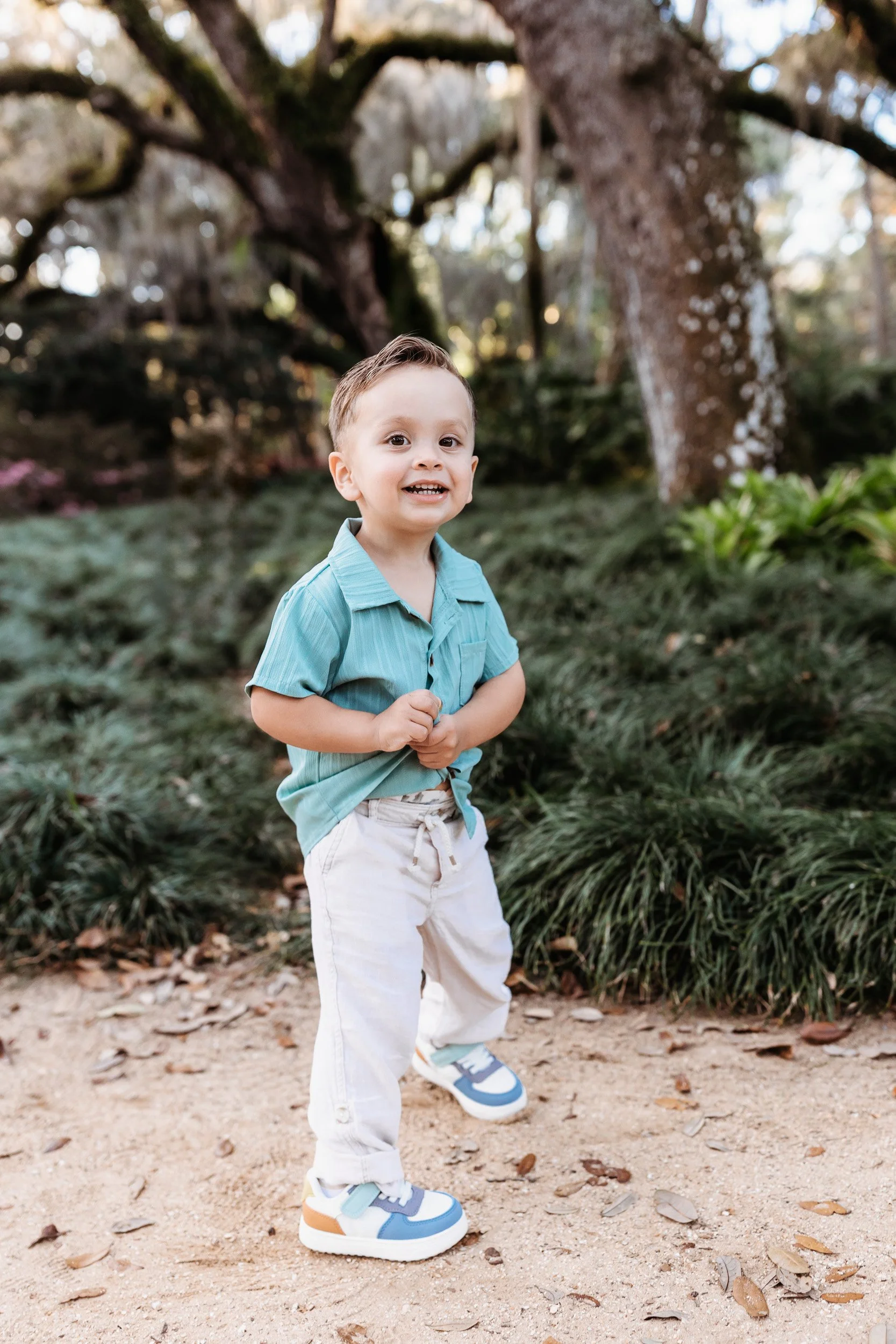 toddler boy at a garden in palm coast for family photos and he is wearing a sage green textured pants and linen pants