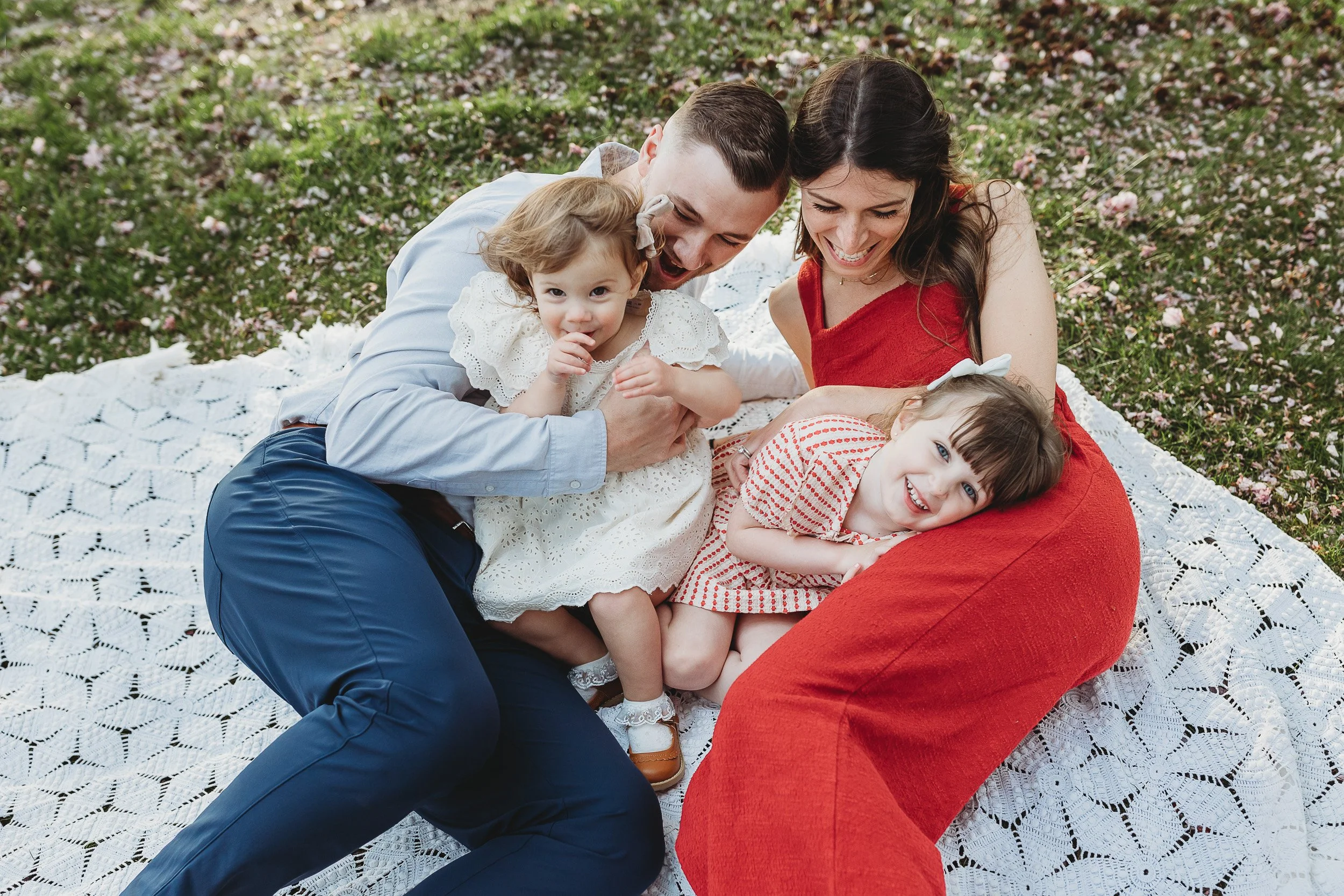 family laying on top of each other on a vintage crochet blanket for spring family photos in a park in Jacksonville and they are all laughing