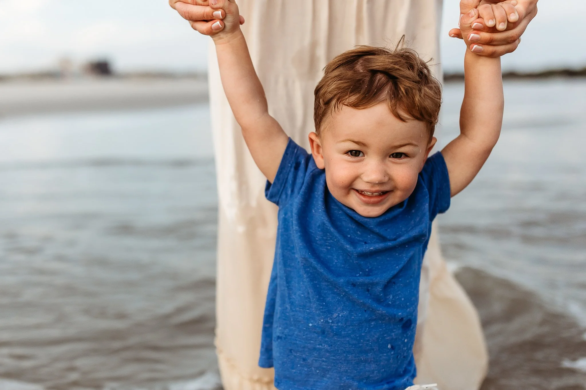 little boy laughing while mom holds his hands 