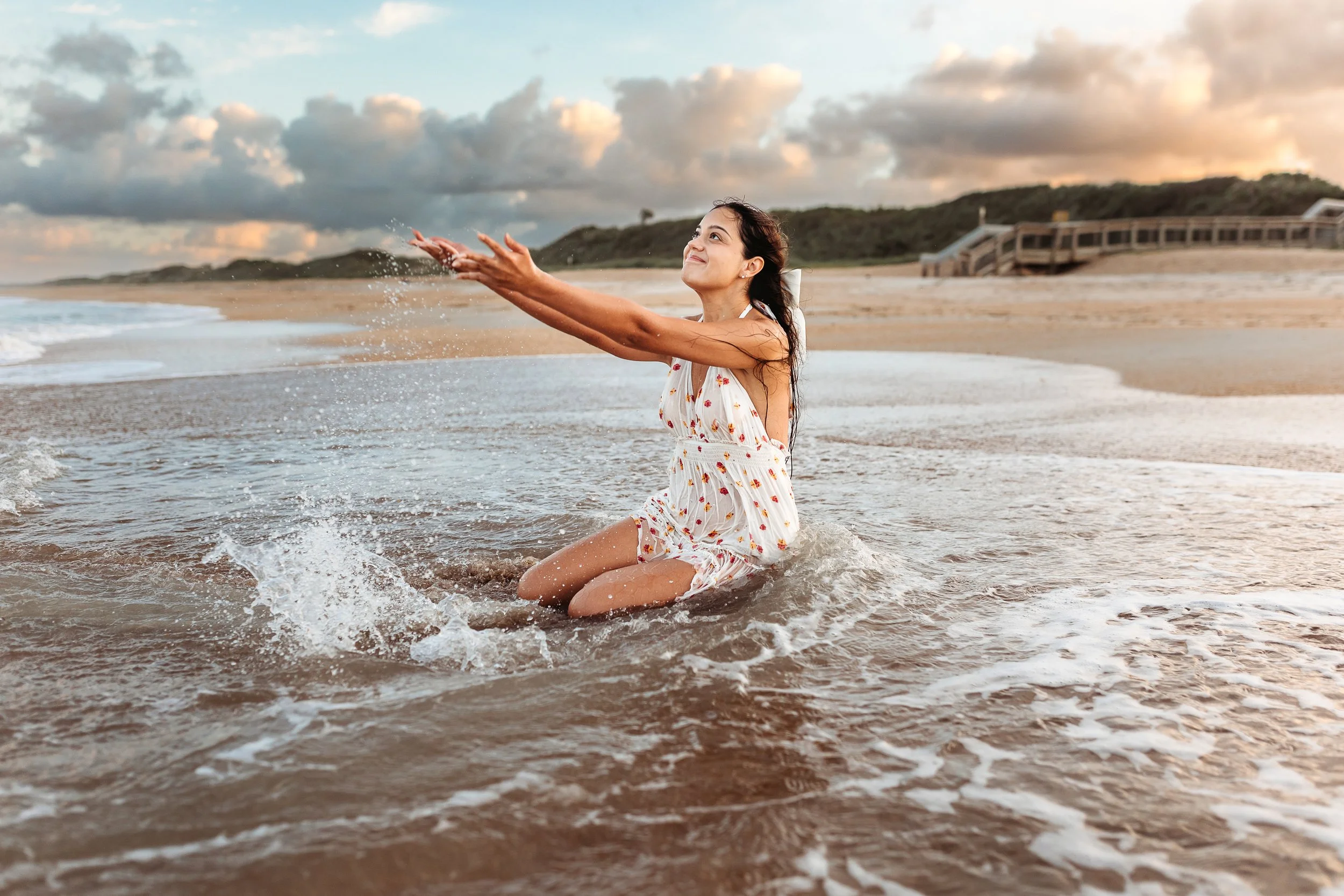 girl splashing water Rin the ocean and she is state din the water looking up to sky with white bow in her hair