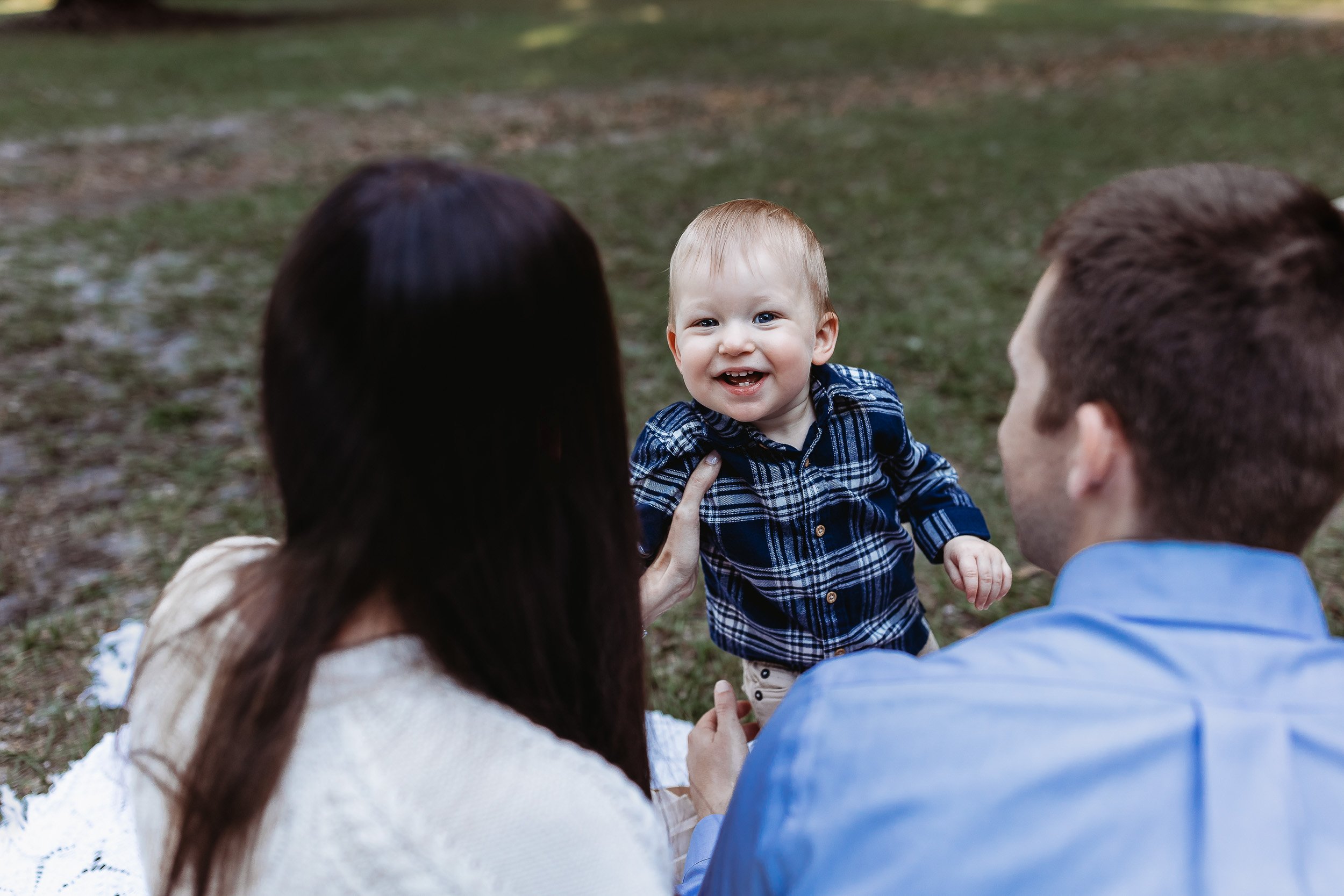 family looking at a boy in a flannel shirt and he is laughing for his photos at a park in Jacksonville