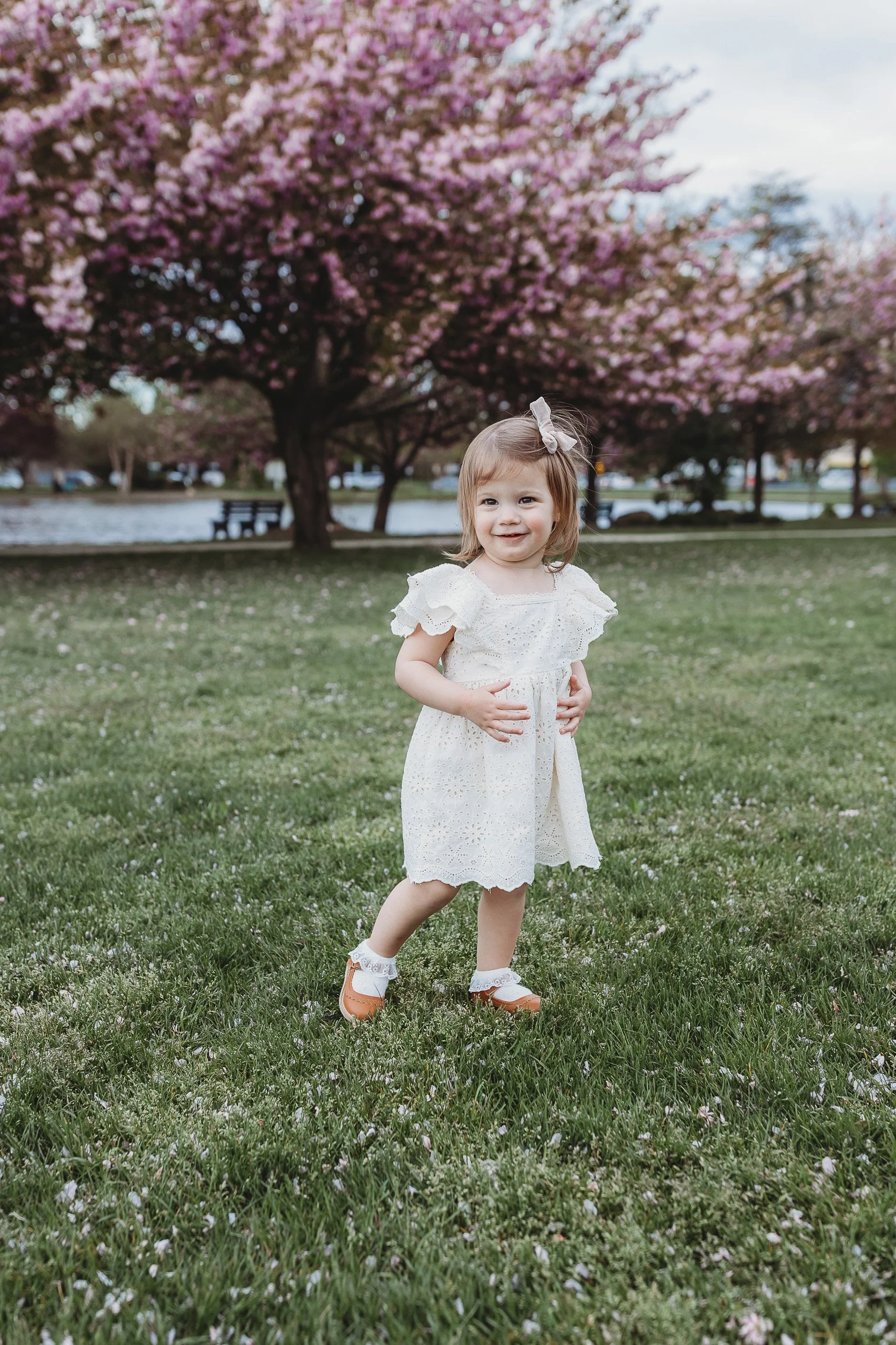 portrait of a toddler girl walking and looking in the distance in a Jacksonville park for family photos and she is wearing a cream eyelet vintage style dress