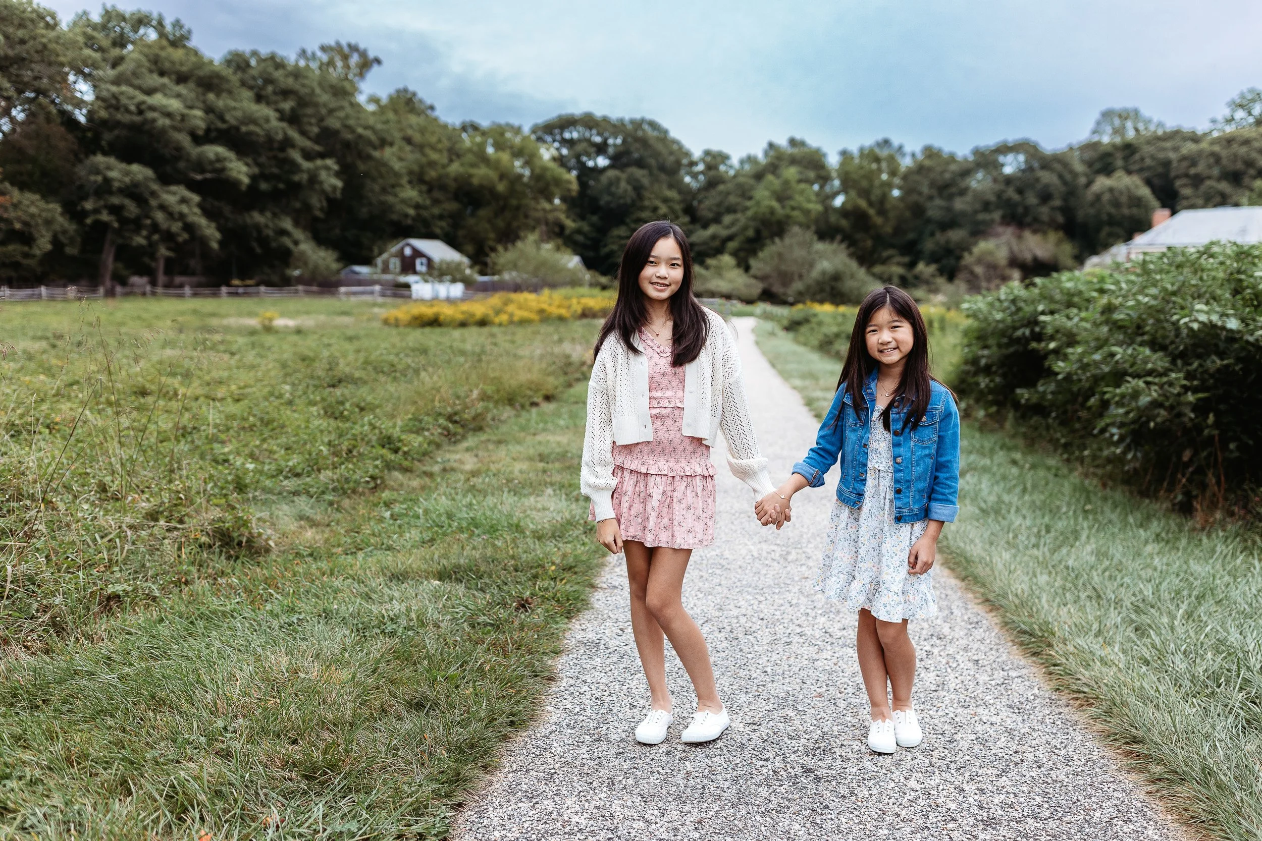 sisters at congaree and penn in spring outfits holding hands on a path and laughing for their family photos