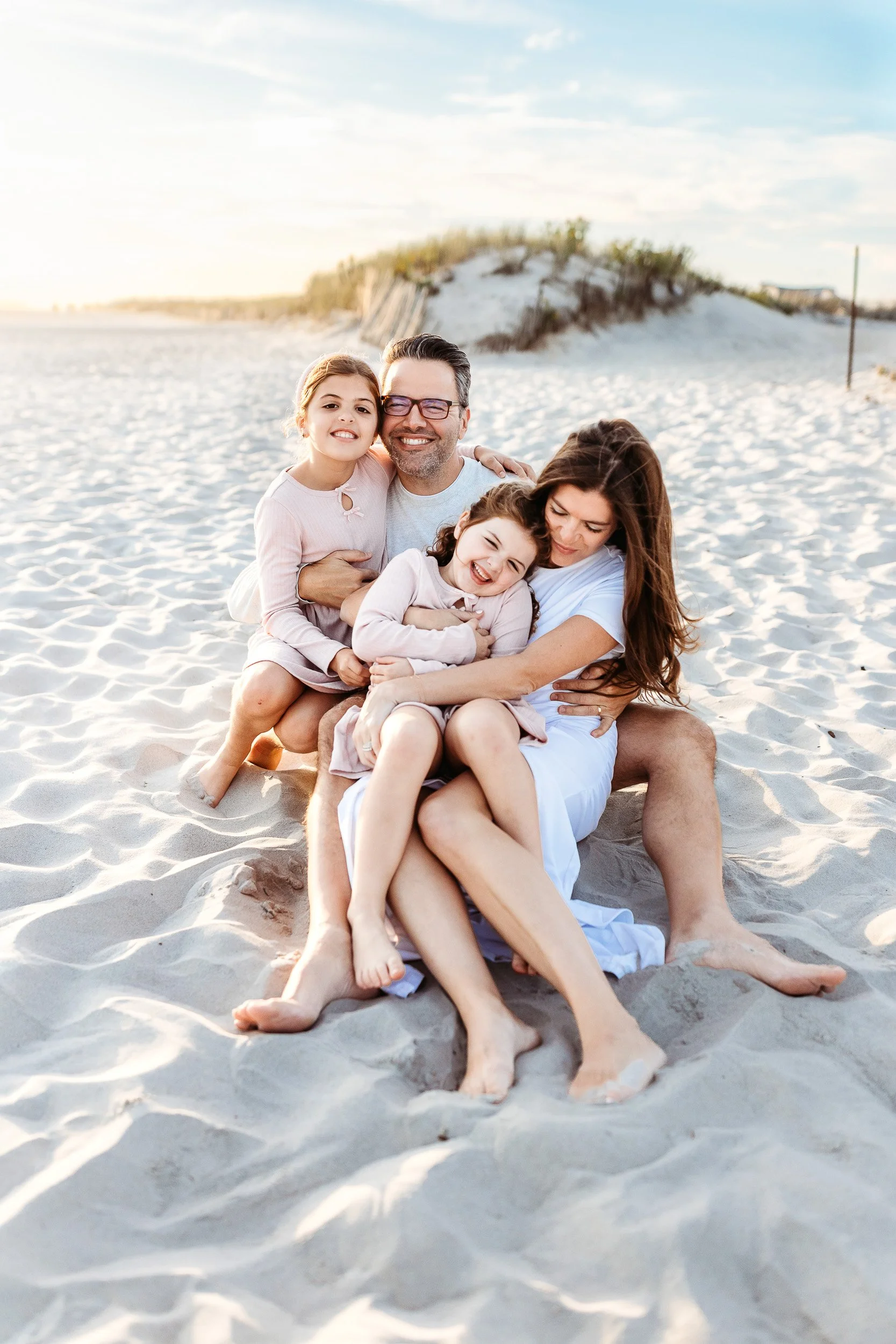 A family of four sitting on the beach, smiling and hugging during sunset.