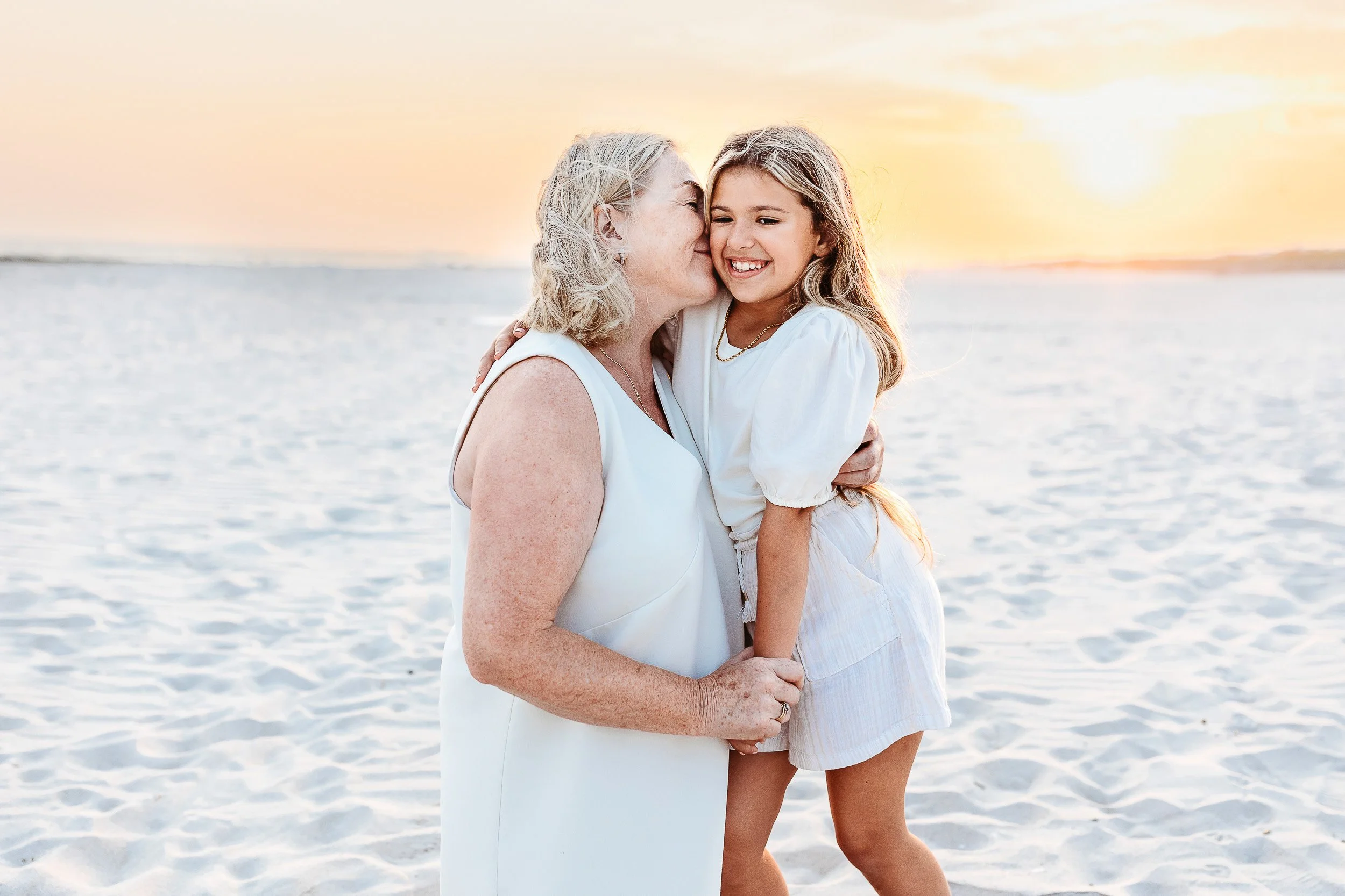 grandmother and granddaughter on the beach in Jacksonville Beach.  Grandma is kissing her granddaughter