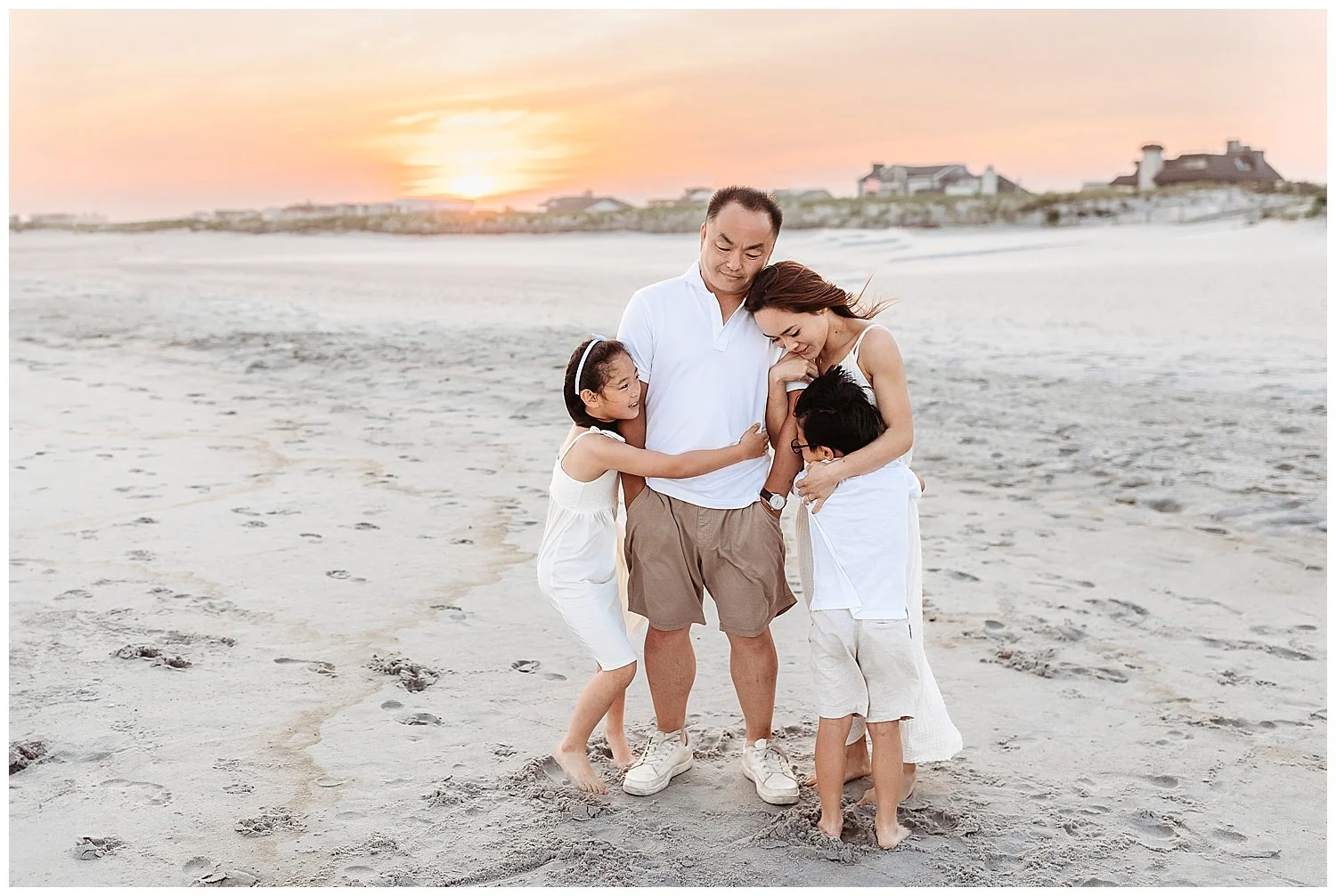 family at the beach at sunset embraced with golden sunset sky wearing tan and white
