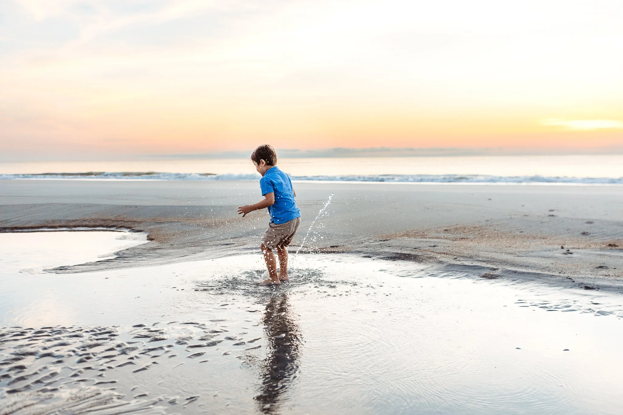little boy jumping in a puddle on the beach ay sunrise with water splattering everywhere