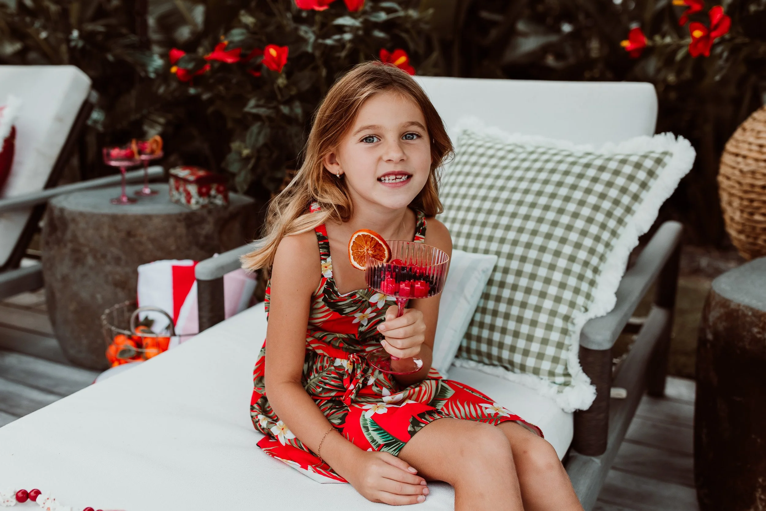 little girl sitting on a chaise lounge in her home in Ponte vedra Florida for holiday photos in a tropical red and green dress
