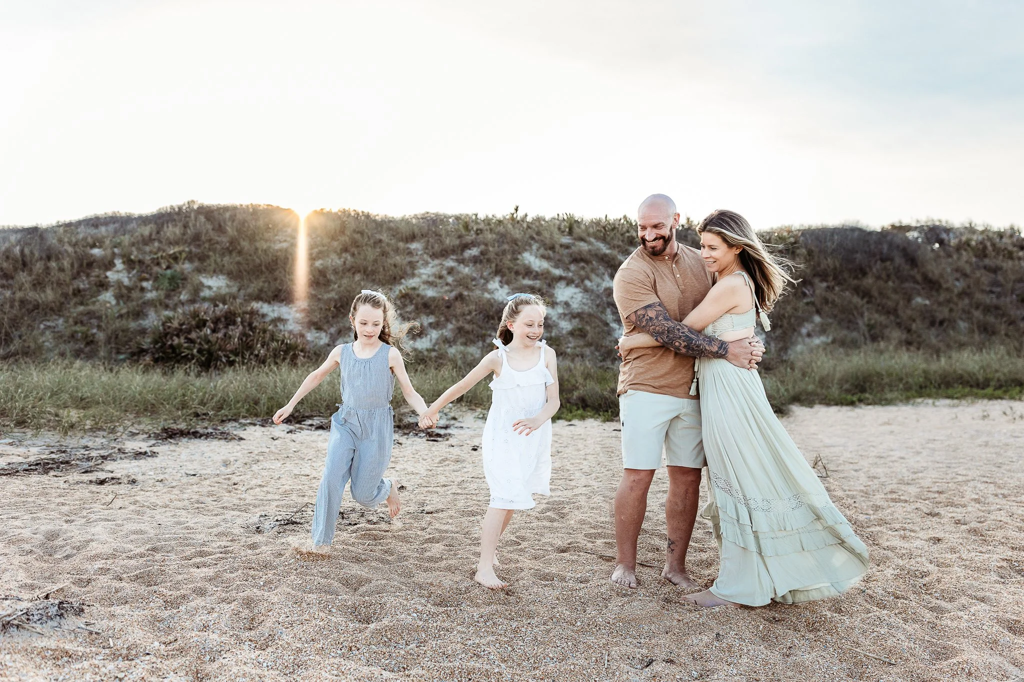 little girls running down a dune while their parents are embraced and watch them