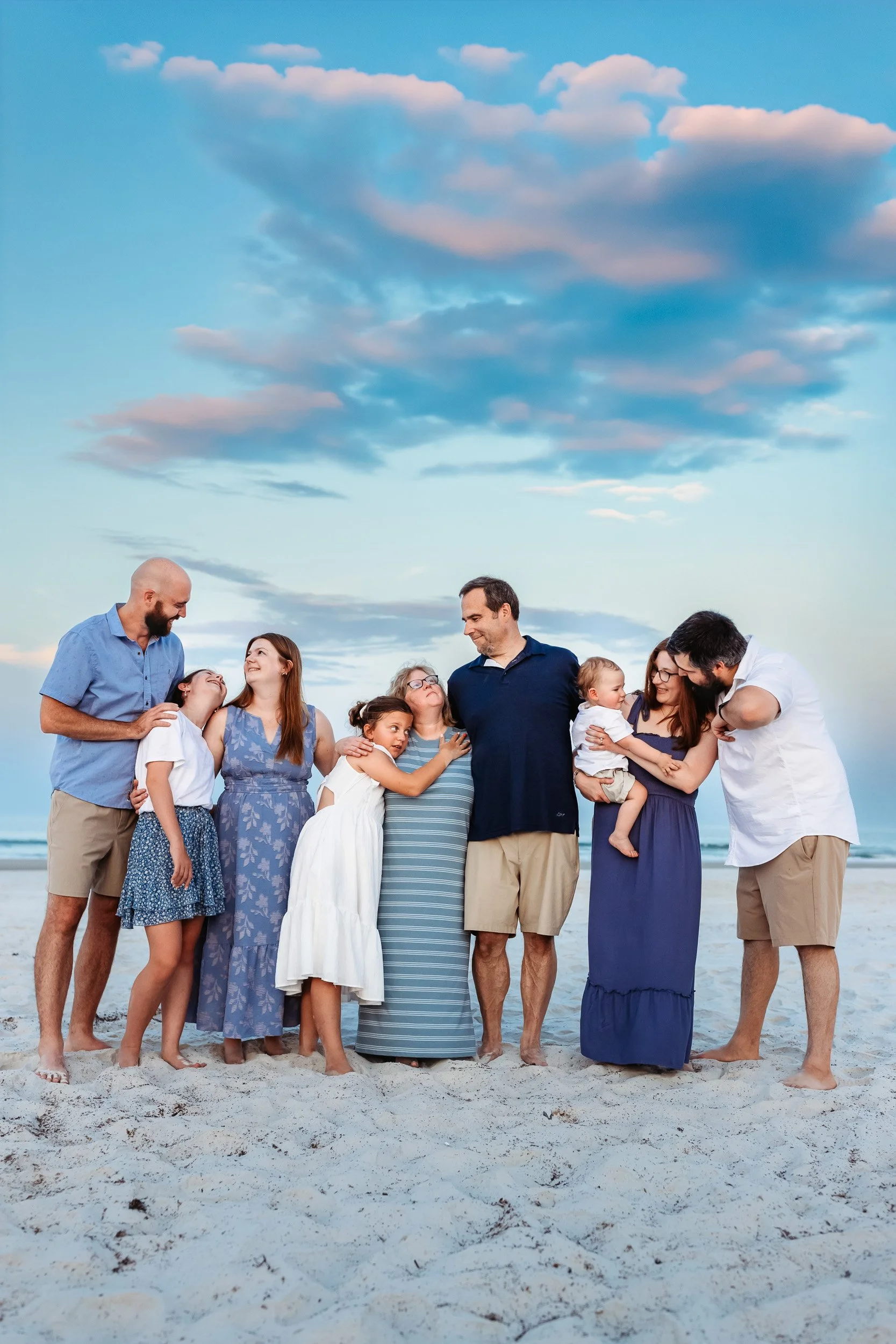 family embraced on the beach at sunset with a dramatic pink and blue sky