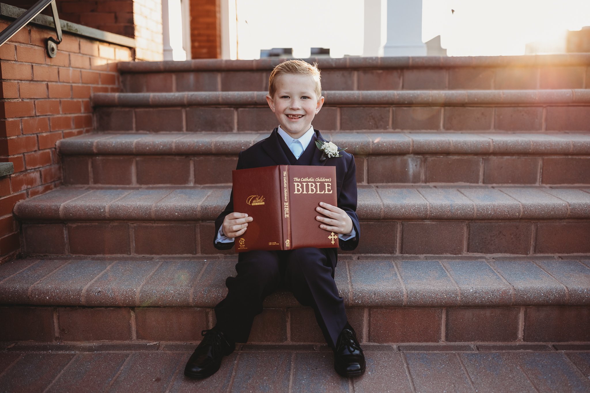 boy seated ib steps at church reading bible at sunset and he is wearing black communion suit