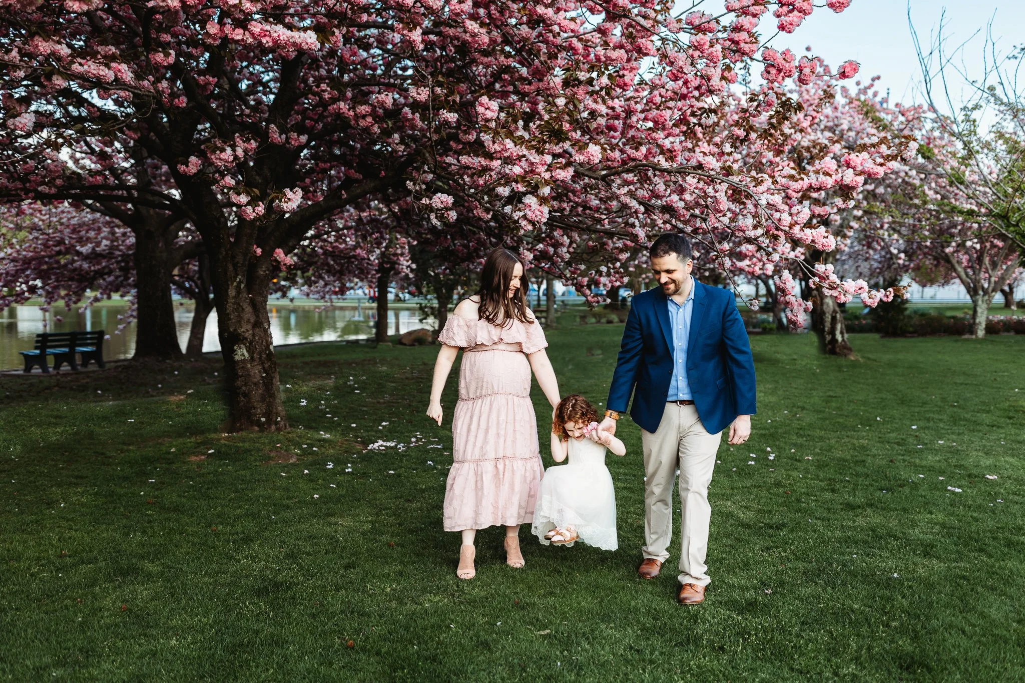 family walking hand in hand and mom is pregnant and there are flowers blooming everywhere