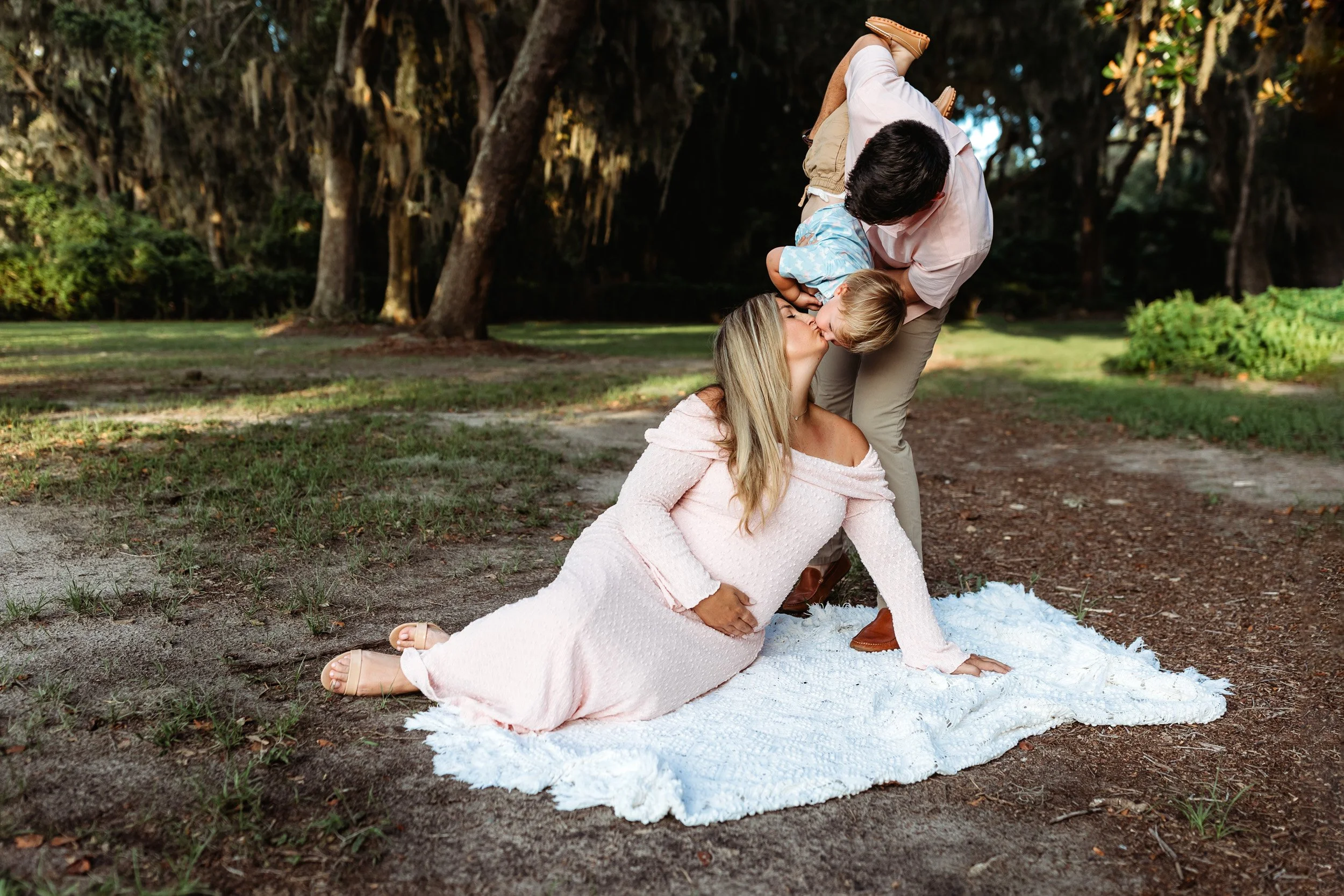 dad air planing a toddler thought the air while mom is seated on a blanket and she kisses him