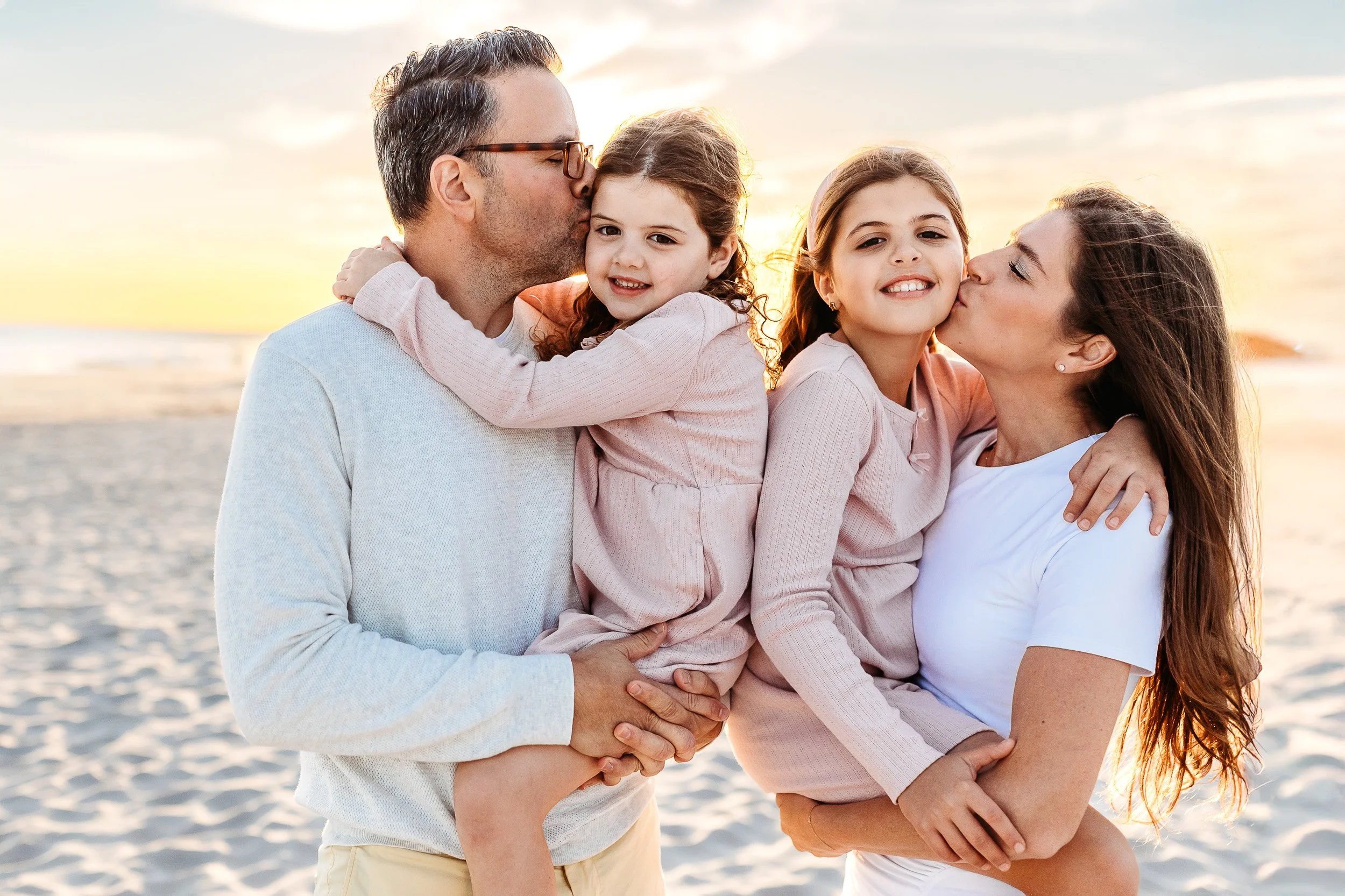 husband and wife kissing their children on the beach at sunset for a beach mini session