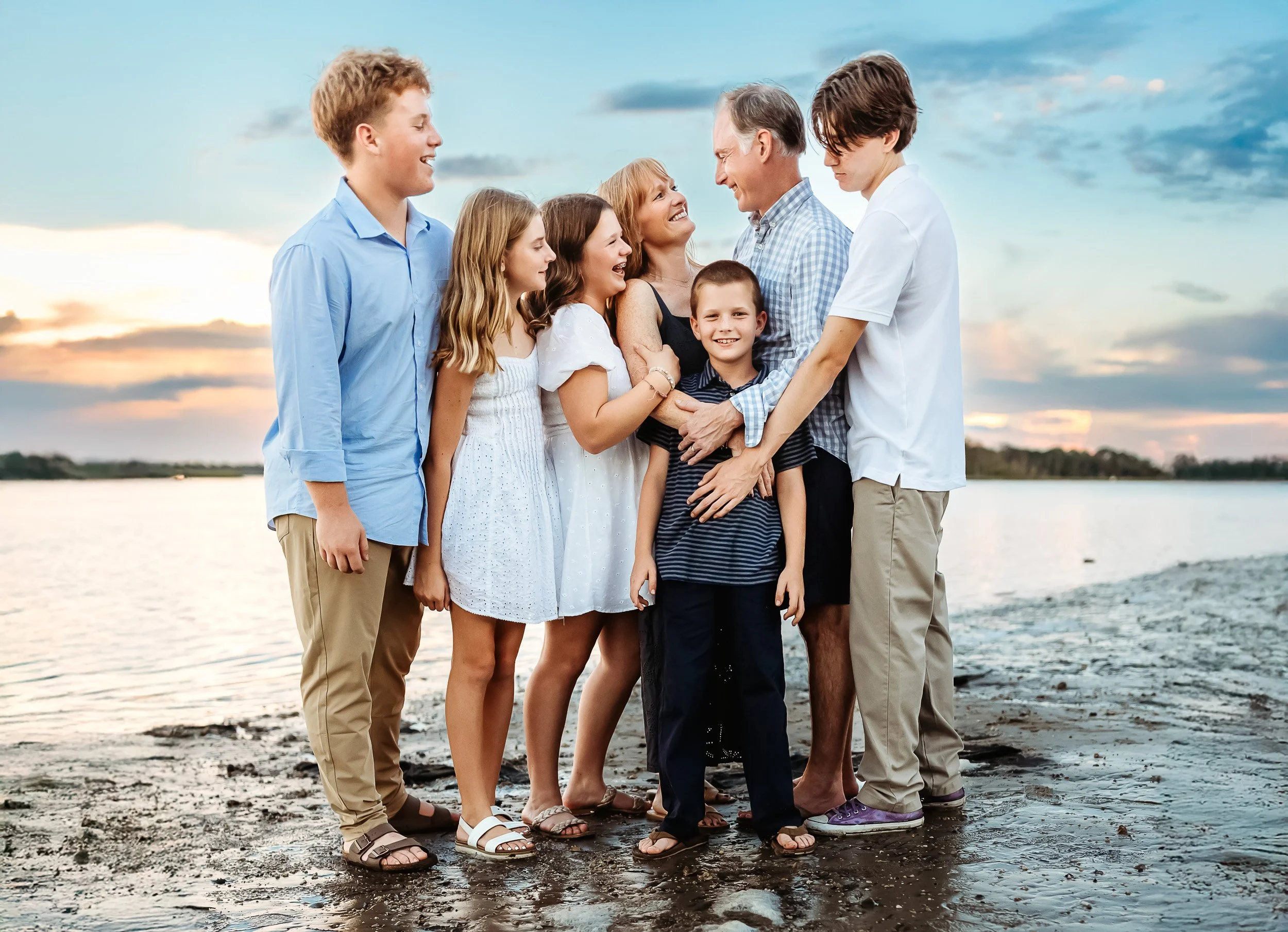 family embraced in the water in blue and grey outfits on the intracoastal for photos with Nocatee photographer at sunset. they are laughing and looking at each other 