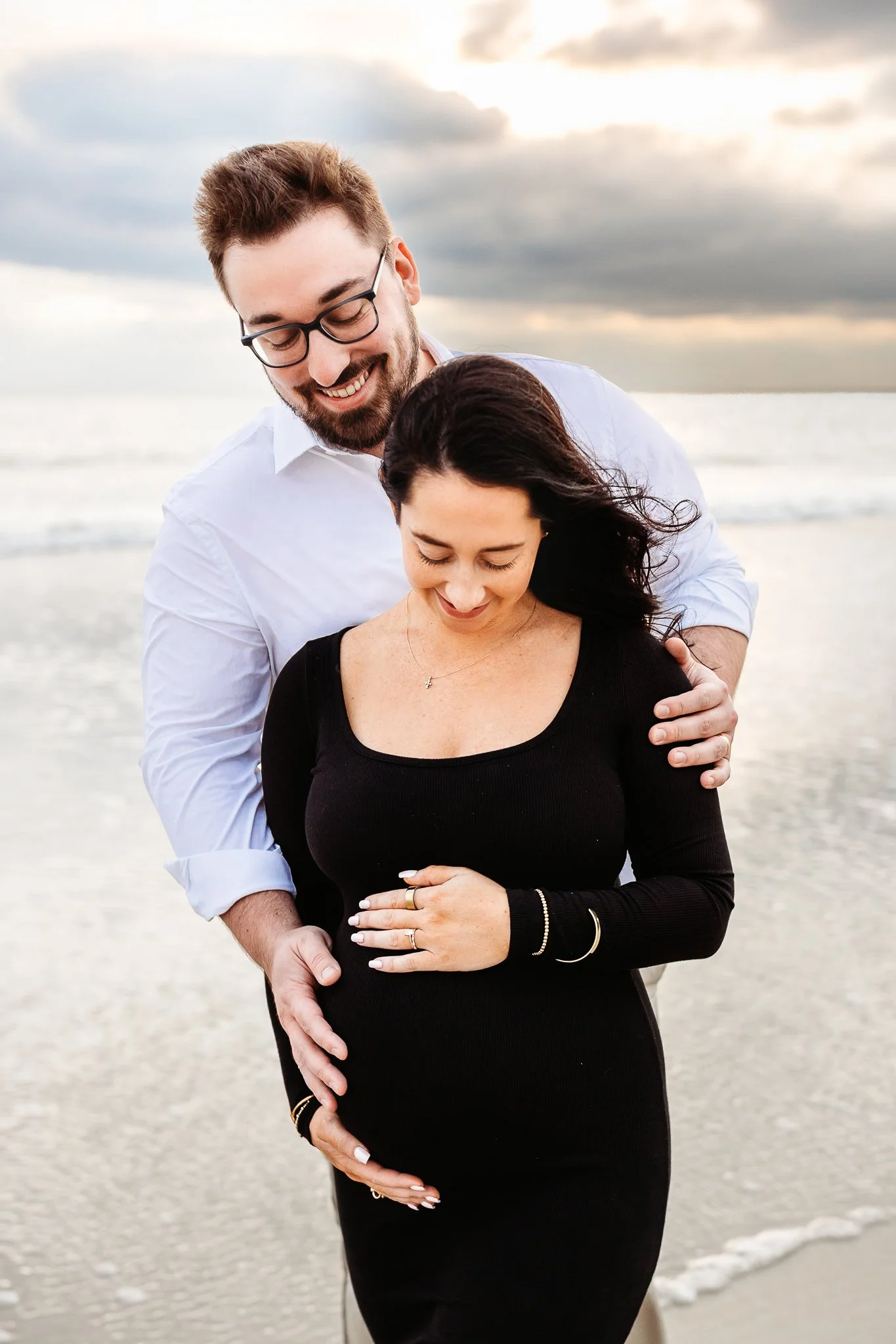 Partner embracing a pregnant mother from behind with both holding her belly.