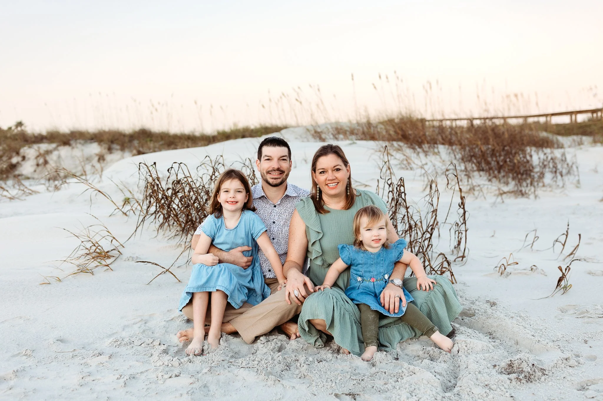Family sitting together near the dunes at Crescent Beach during a relaxed sunrise photography session.