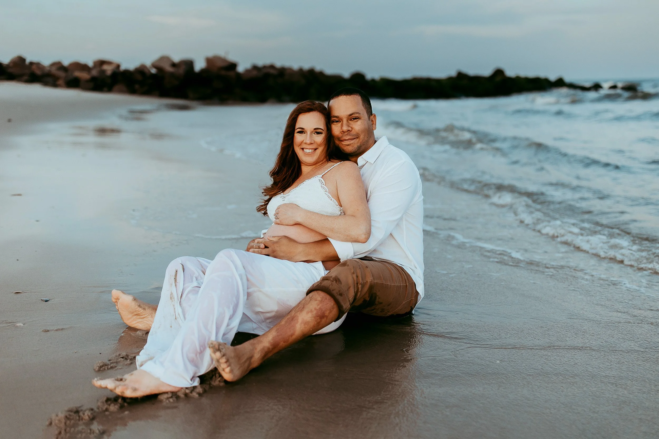couple seated on a beach at sunset during a baby moon vacation for a photo session
