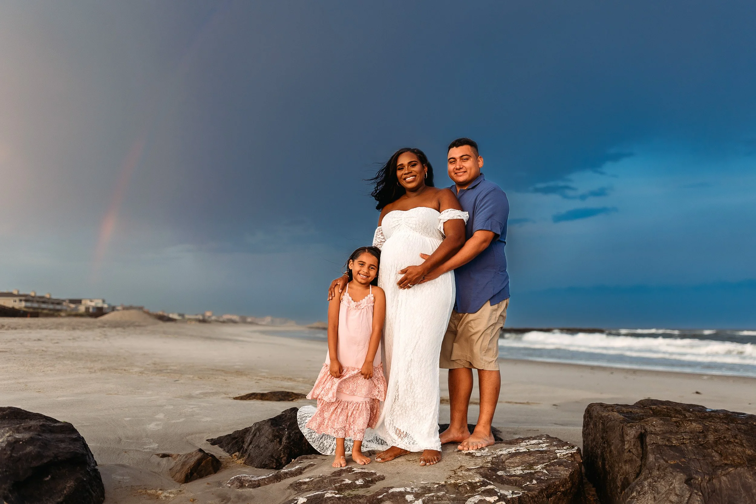 family on a jetty on the beach at there is a rainbow behind them 