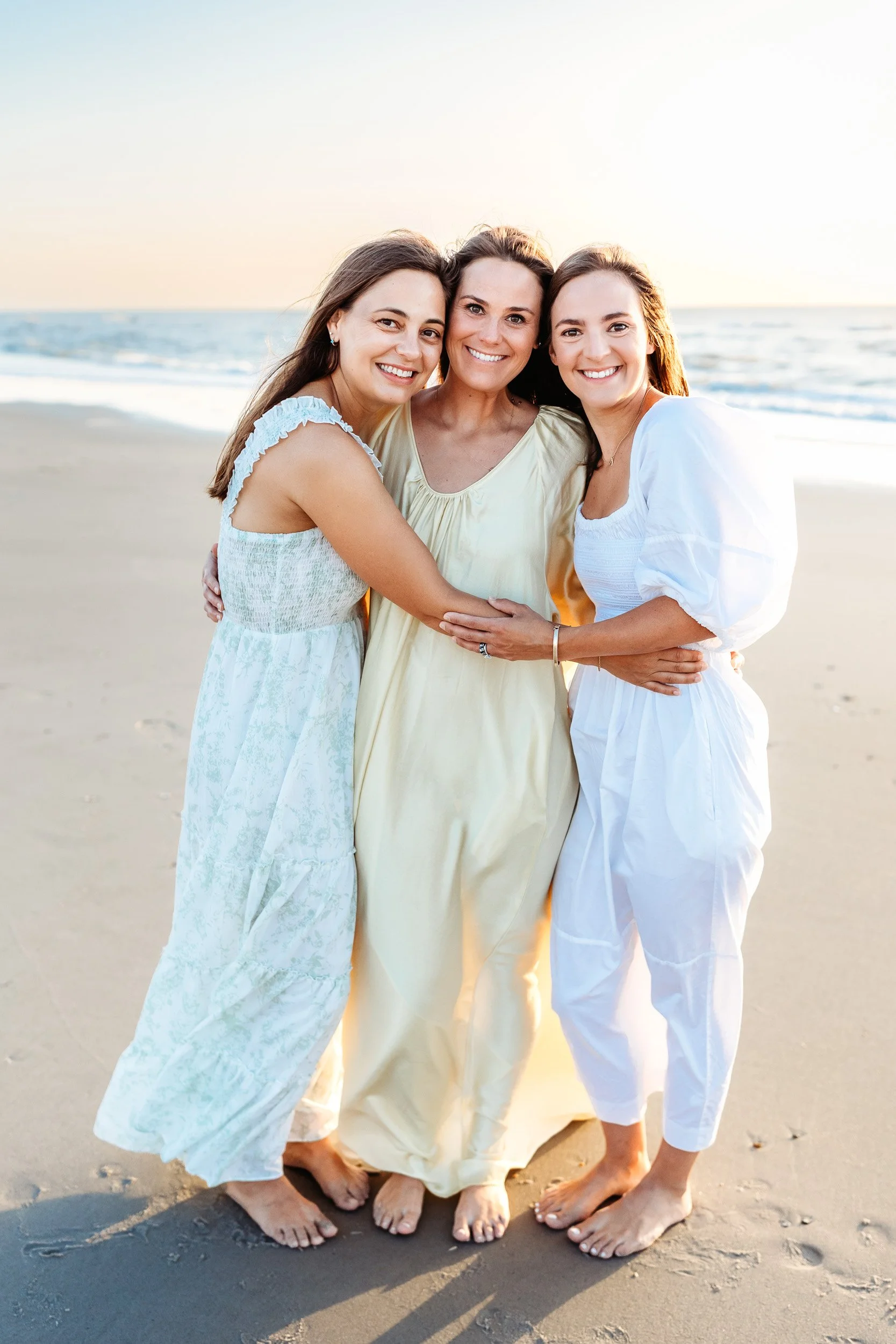 adults sisters embraced on the beach at sunrise wearing white sage and yellow