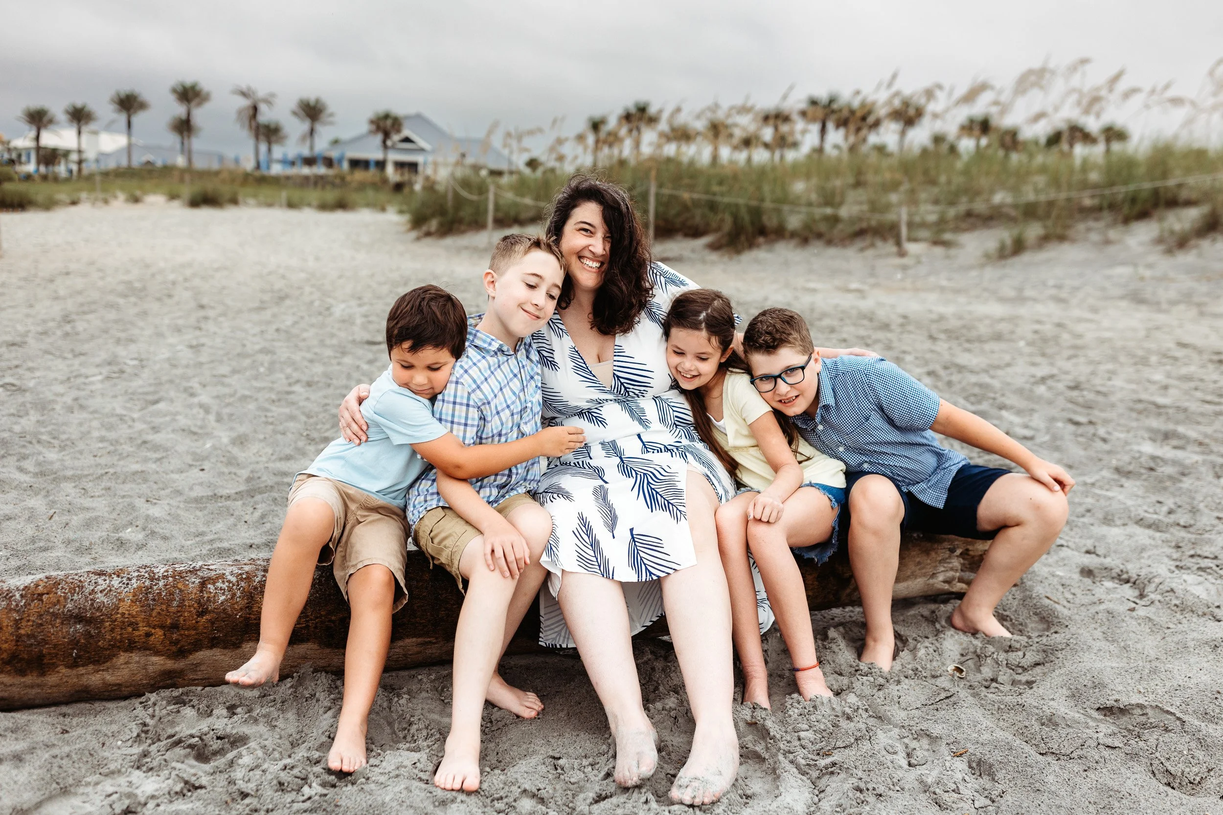 aunt with her nieces and nephews laughing on the beach at sunrise and they are seated on a driftwood