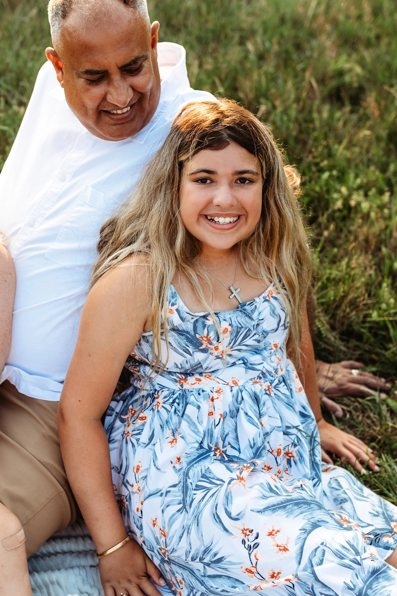 daughter leaning into dad while seated in the grass and dad is looking down at her