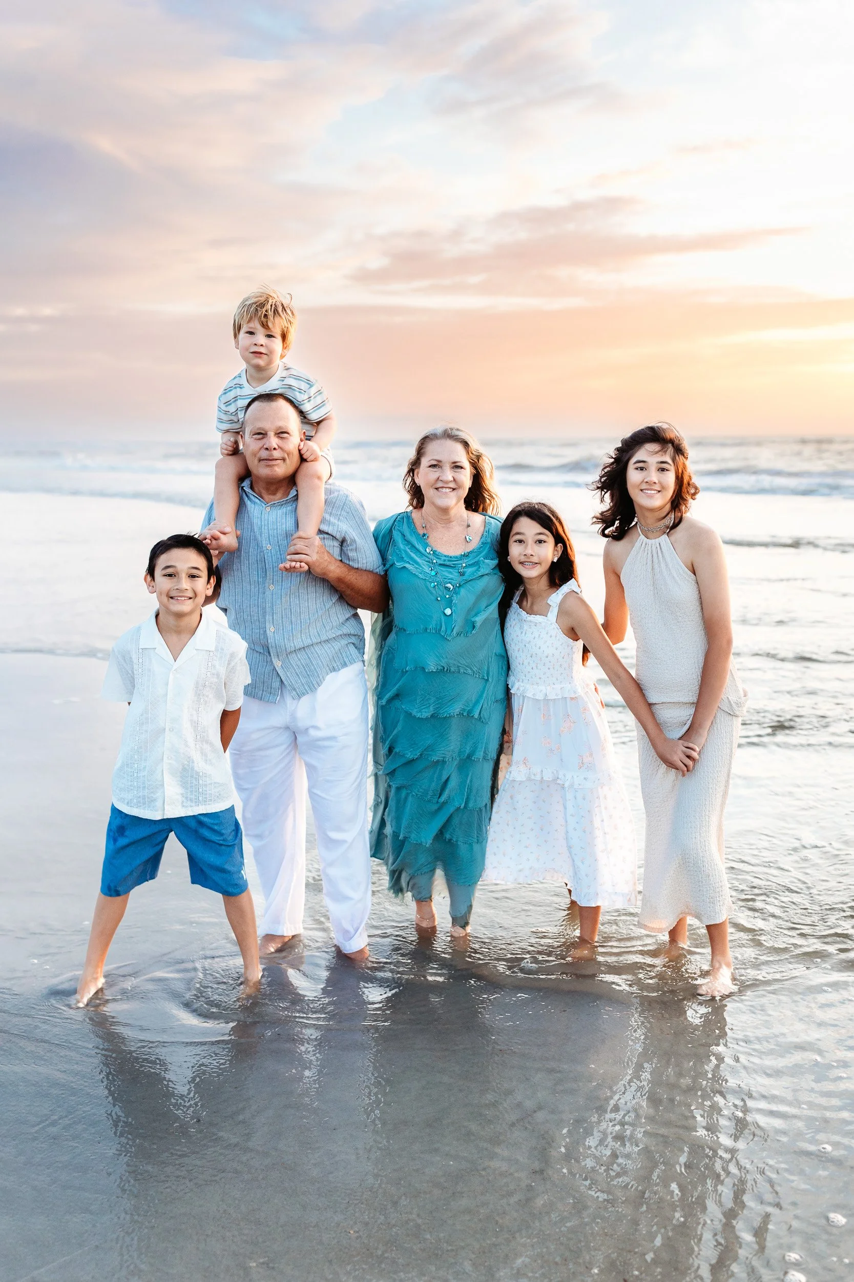 grandparents holding all of their grandchildren on the beach at sunrise
