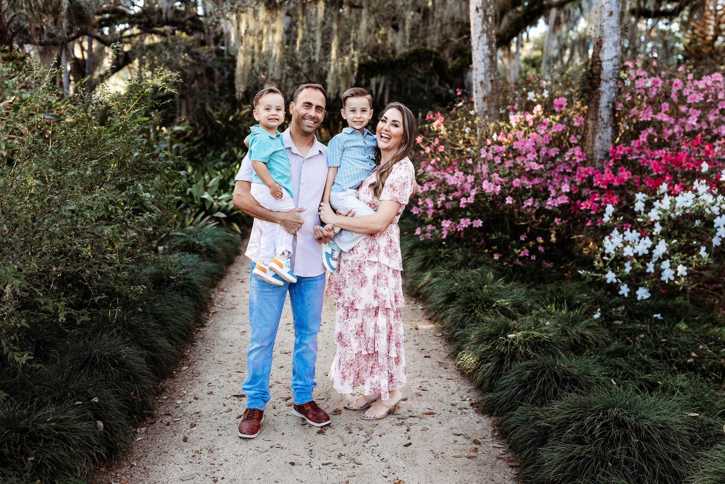 a family dressed in tan pink blue and green in the garden and there are azaleas in bloom around them