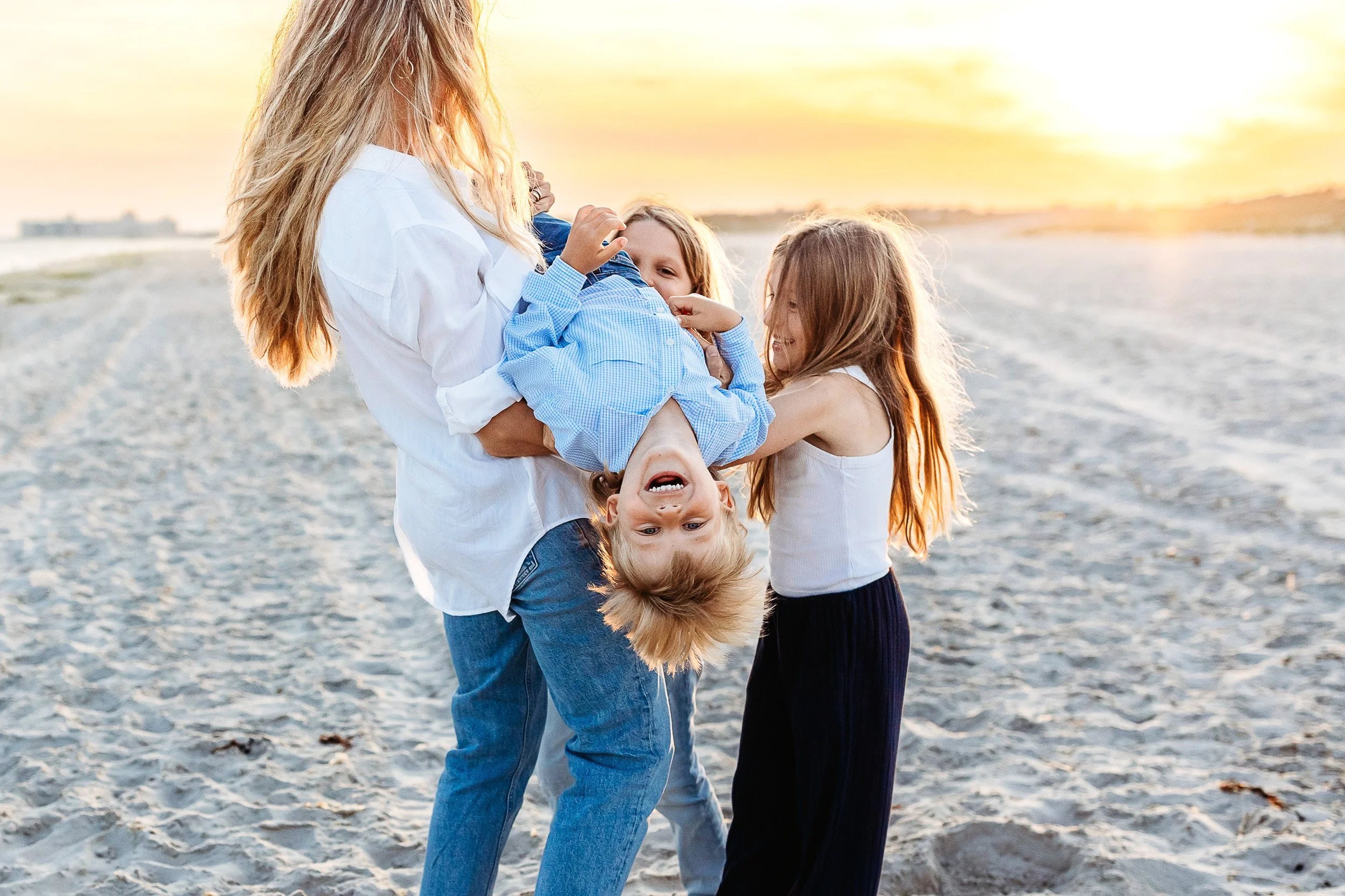 mother holding toddler boy upside down and the other children are tickling him and they are all laughing during family photos on st augustine beach
