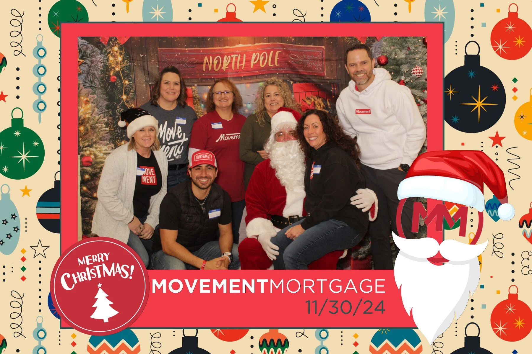 A group of people, including Santa Claus, posing for a photo at a Christmas event with a decorated background, Christmas tree, and a North Pole sign. The group is smiling and wearing holiday-themed clothing.