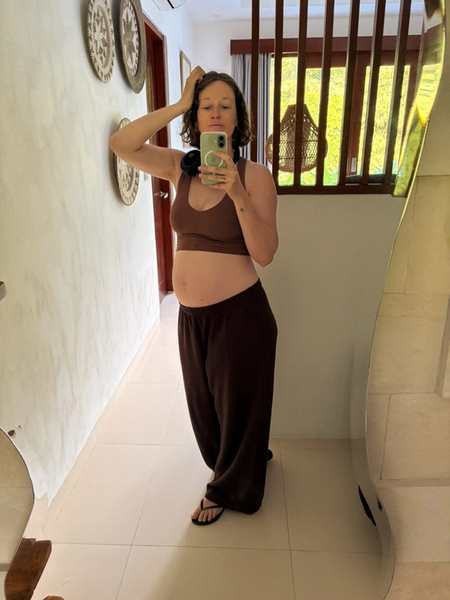 Ella Giljam, pregnant, taking a mirror photo in a sunlit hallway during her baby moon in Indonesia