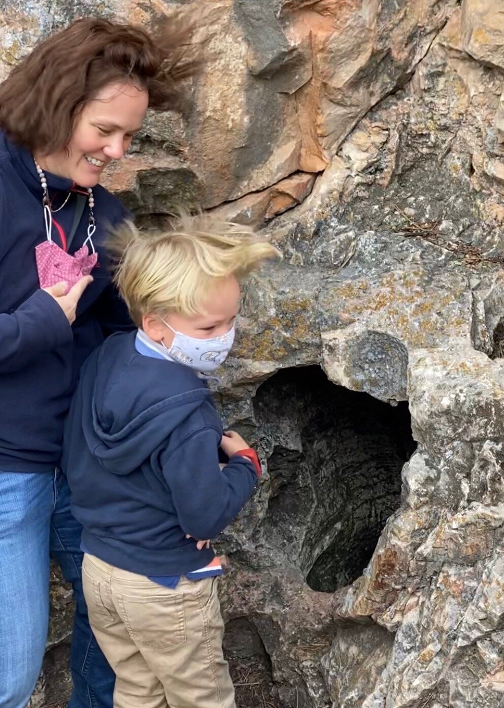 Mama and Popcorn feeling the wind and trying to look down into the first discovered entrance to Wind Cave.  Anyone want to climb down that?  Screenshot by Karen from video by Jude Boudreaux, May 26, 2021