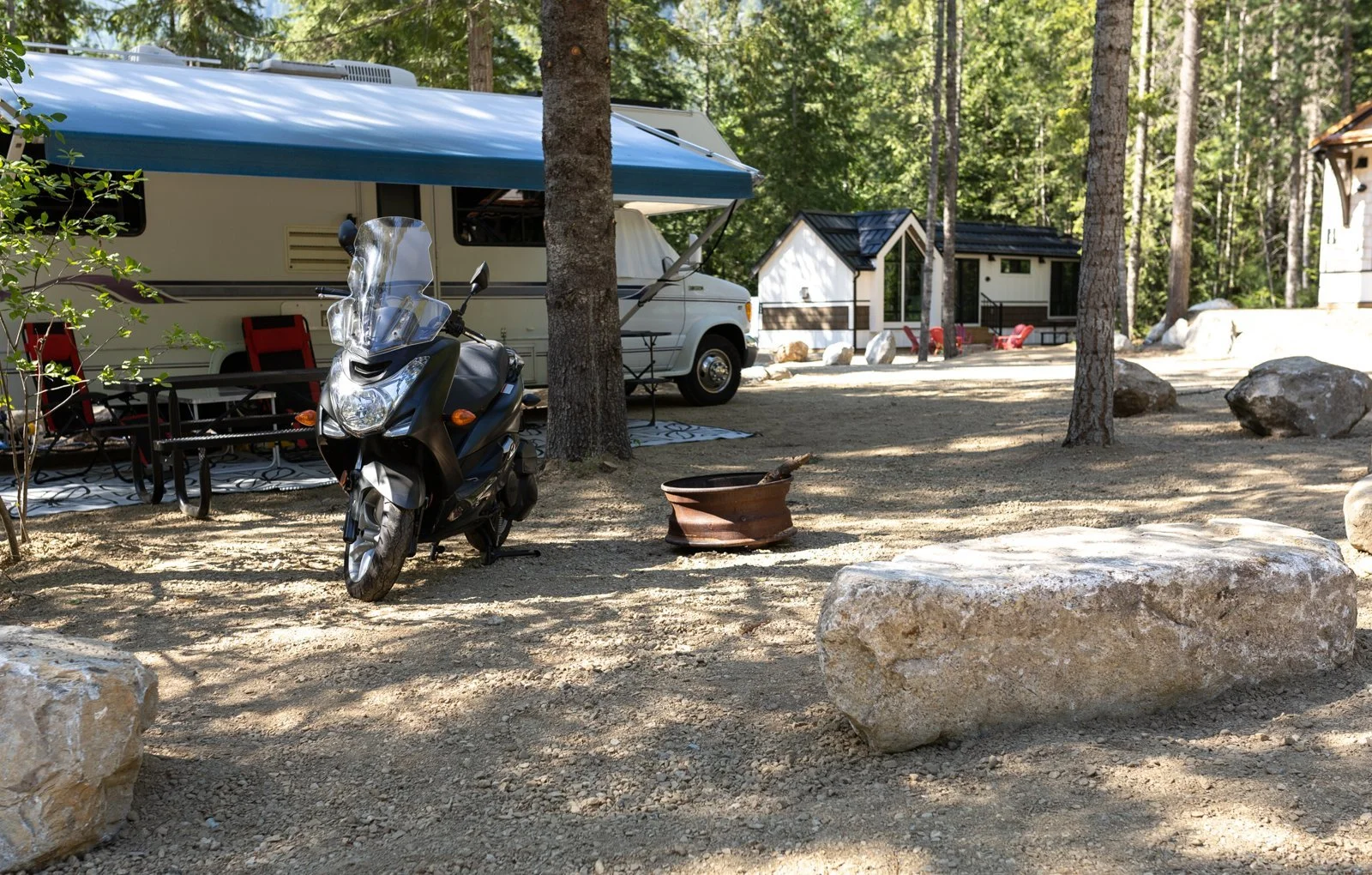 RV parked at a forested Crazy Creek campsite, with one of the cabins just behind