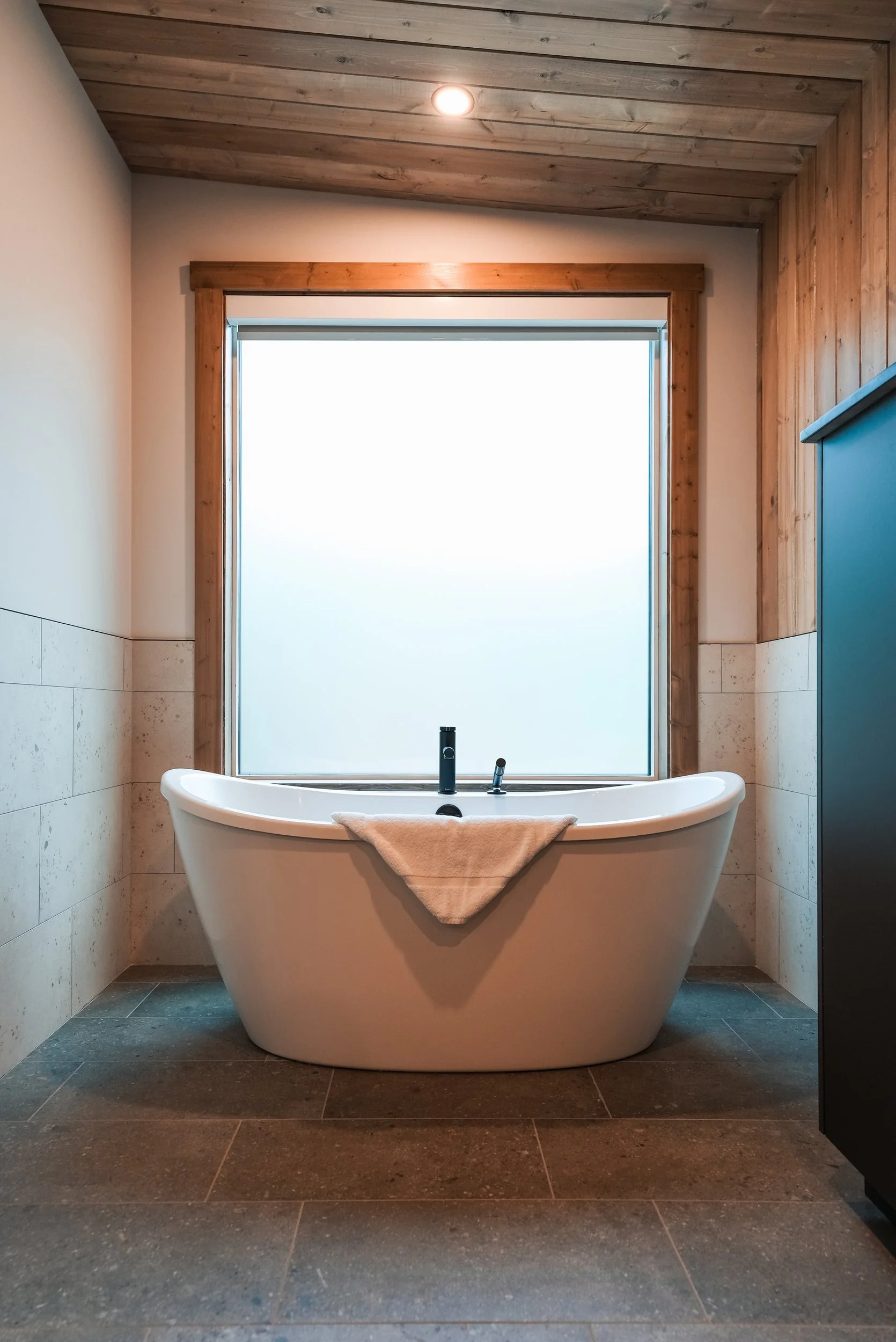 Freestanding soaker tub below a large frosted window in the Nest