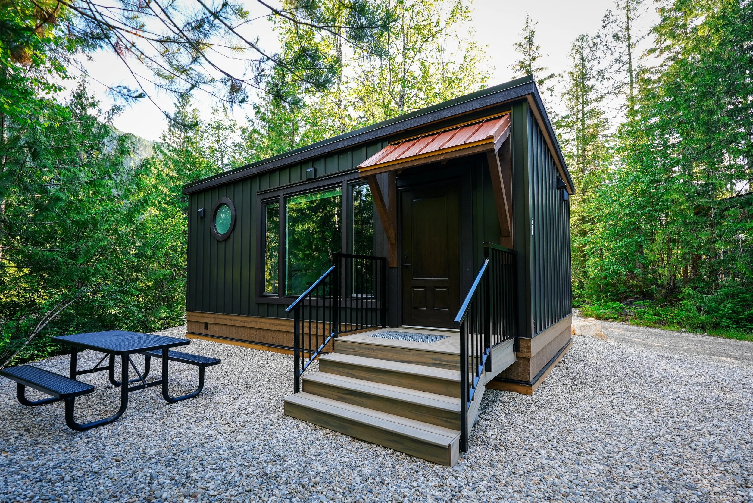 Nest cabin exterior with dark board-and-batten siding, a copper awning and a picnic table among the trees