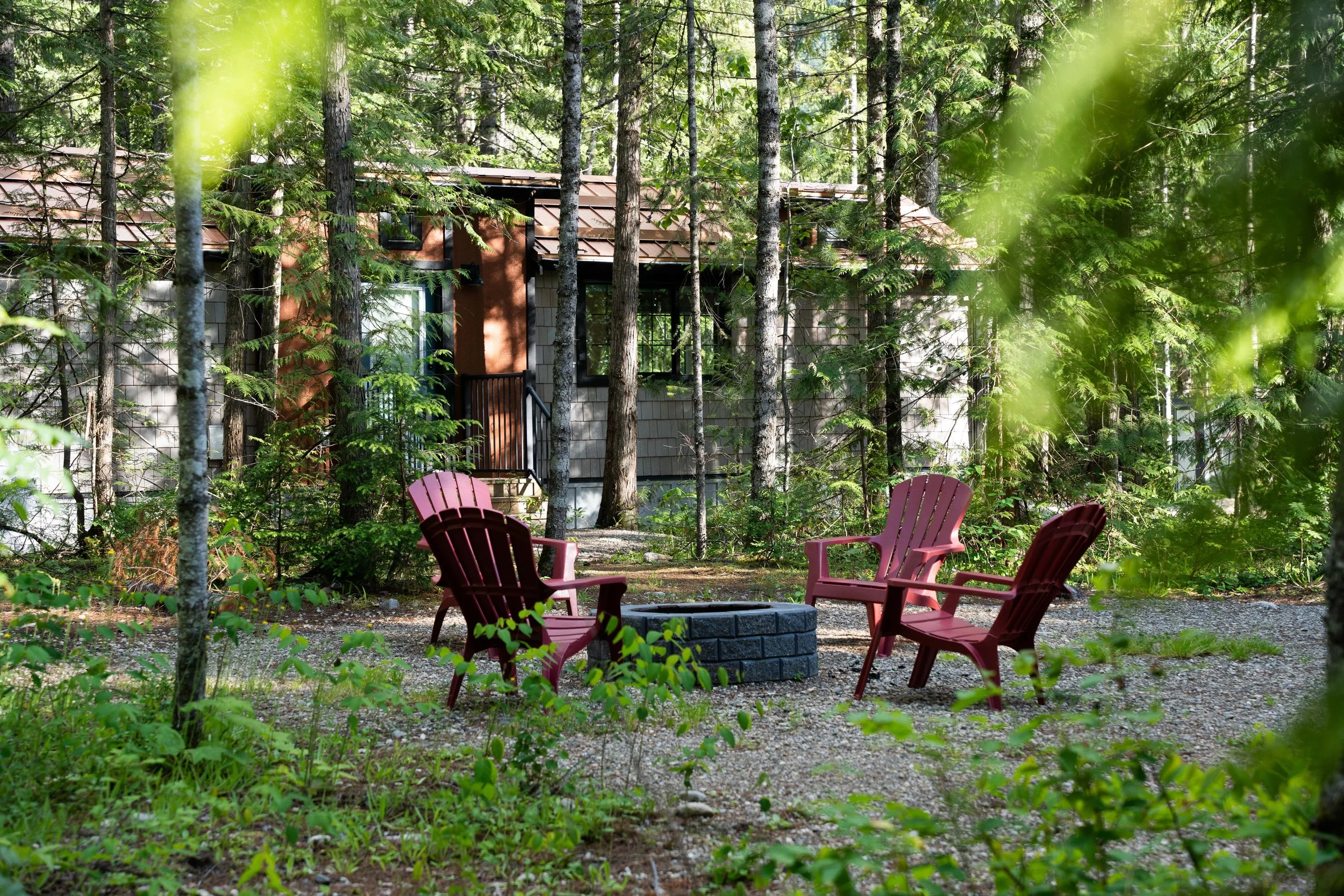 Red Adirondack chairs around a stone fire pit in the trees beside the Elkhorn